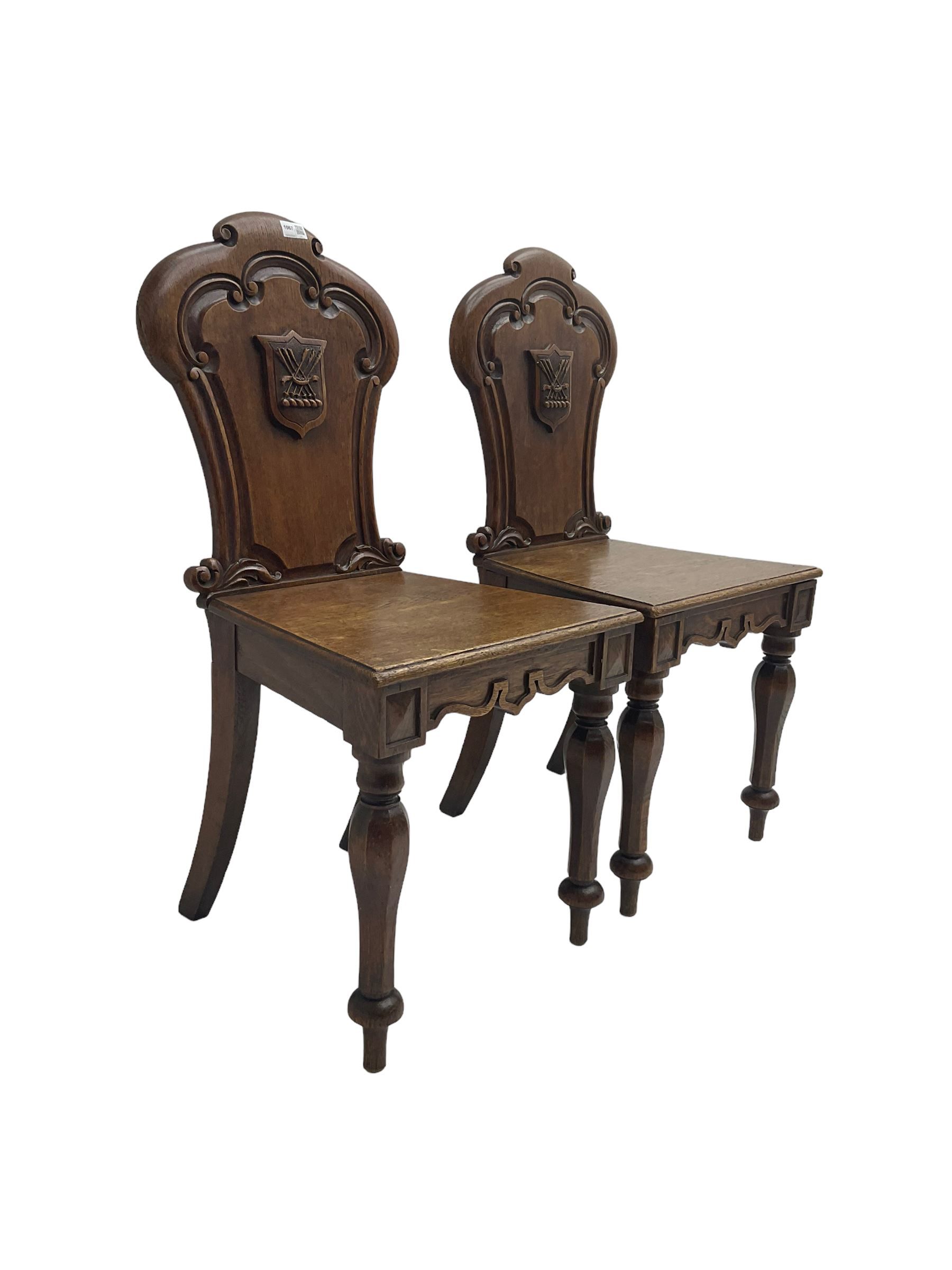 Pair Victorian oak hall chairs, scallop shaped back with carved scrolls and central shield moulding, panel seat over shaped frieze rail, raised on turned supports