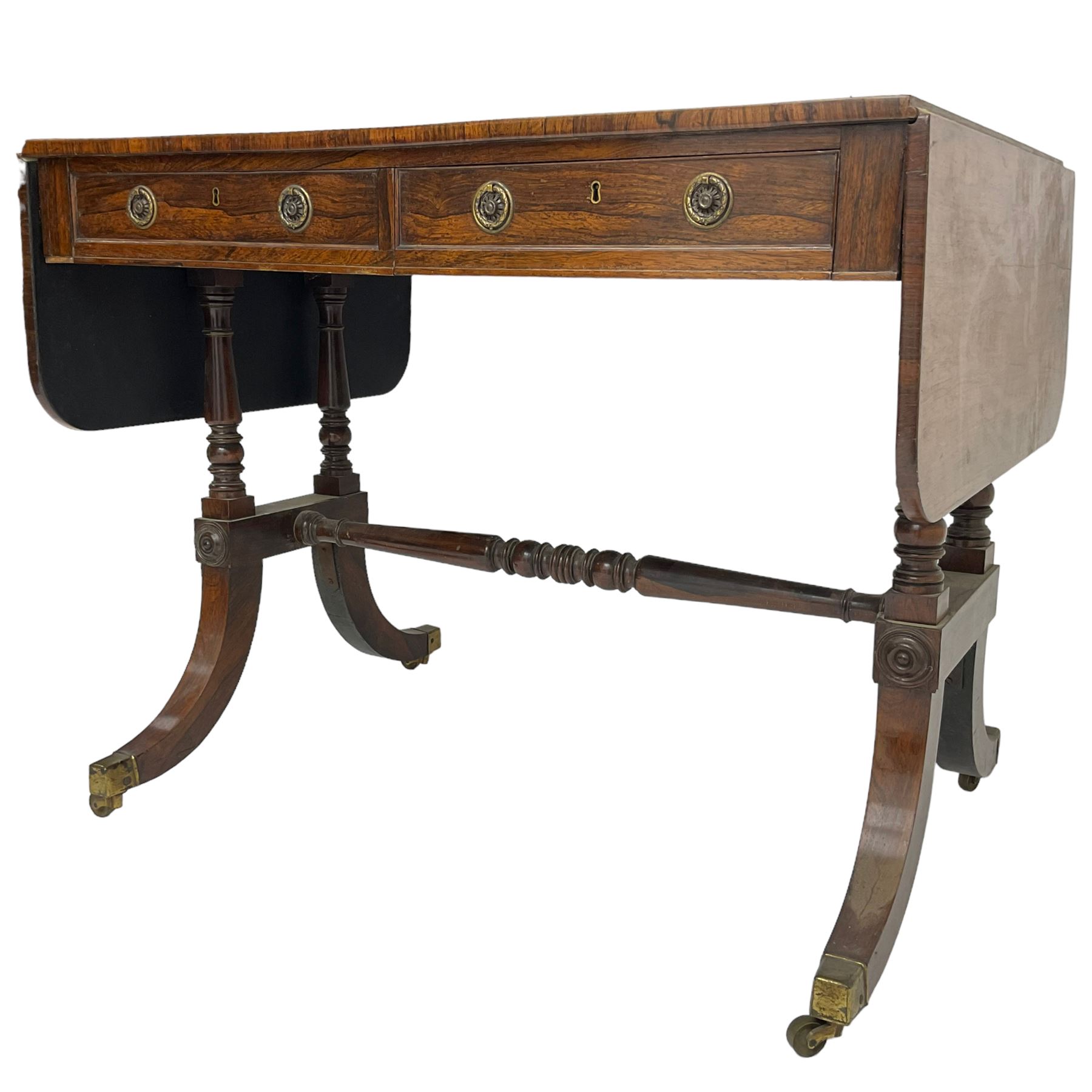 Regency rosewood sofa table, drop leaf rectangular top with rounded corners, fitted with two drawers and two opposing false drawers, raised on dual turned columns terminating in splayed feet united by turned stretcher, on brass cups and castors