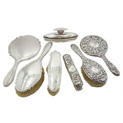 Matched four piece early 20th century silver mounted dressing table set, comprising hand held mirror, hair brush, clothes brush, and buffer in glass stand, of plain form, hallmarked Birmingham 1924 and 1925, and Edinburgh 1923, various makers marks, together with a 1950's three piece silver mounted dressing table set, comprising hand held mirror, hair brush and clothes brush, with embossed scrolling foliate decoration throughout, hallmarked W I Broadway & Co, Birmingham 1958