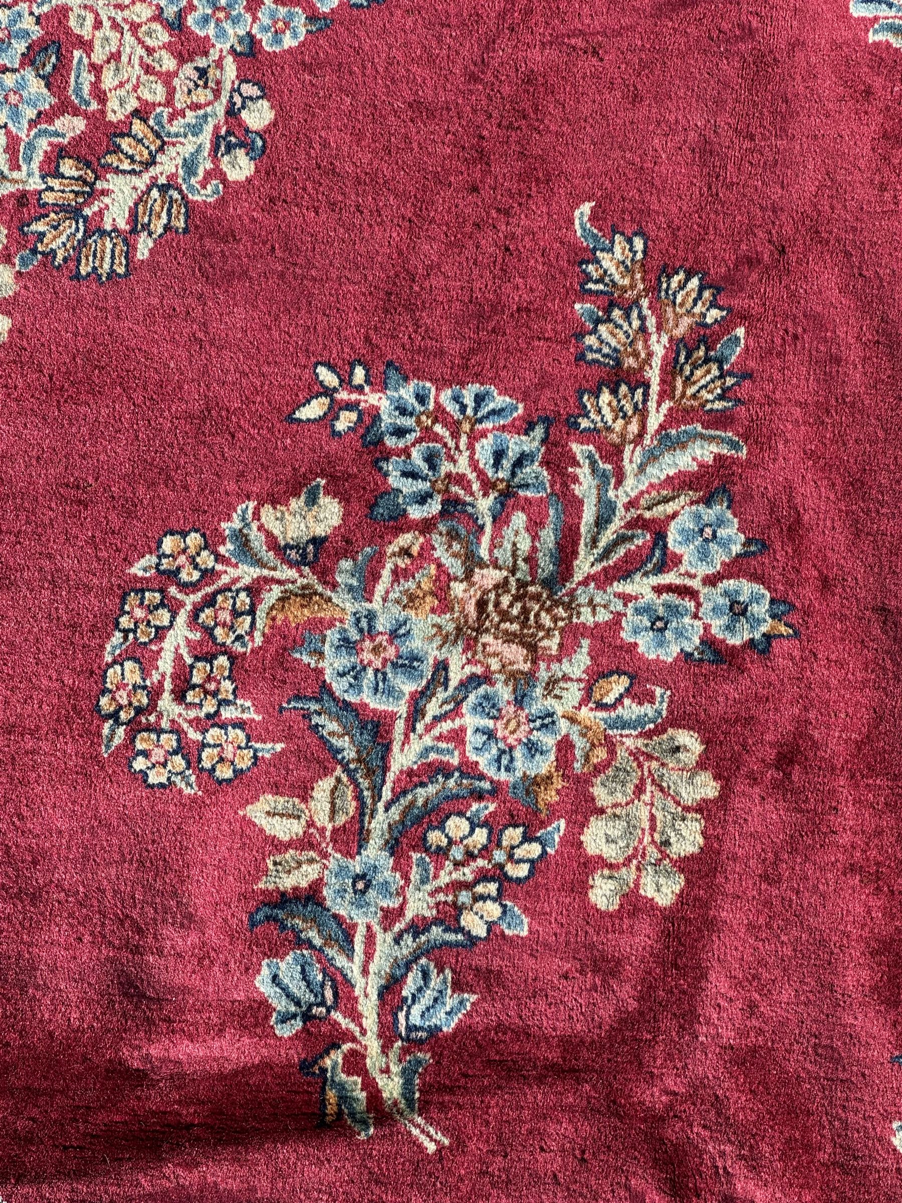 Persian Kirman carpet, the bold ruby field hosting a multi-lobed central medallion, embellished with scrolling vines and floral sprays, edged by layered borders and trimmed with short fringe