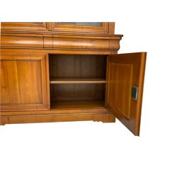 French cherry wood bookcase on cupboard, projecting cornice over two cupboard doors with bevelled glass panels enclosing three adjustable shelves, base fitted with two cushion drawers over double cupboard