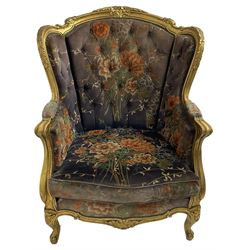 Pair of Louis XVI design gilt framed wingback armchairs, cresting rail carved and moulded with foliate decoration and C-scrolls, upholstered in buttoned floral patterned mauve velvet with loose seat cushion, scallop carved apron over cabriole supports