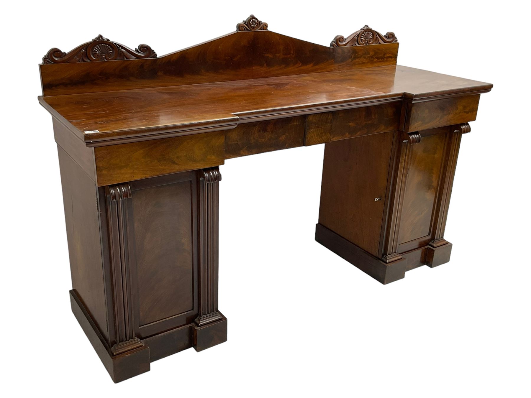 Early 19th century mahogany reverse break-front twin pedestal sideboard, raised back carved with cartouche and rosette detail with extending scrolling, fitted with two frieze drawers, the flanking panelled cupboards enclosing sliding trays and cellarette drawer