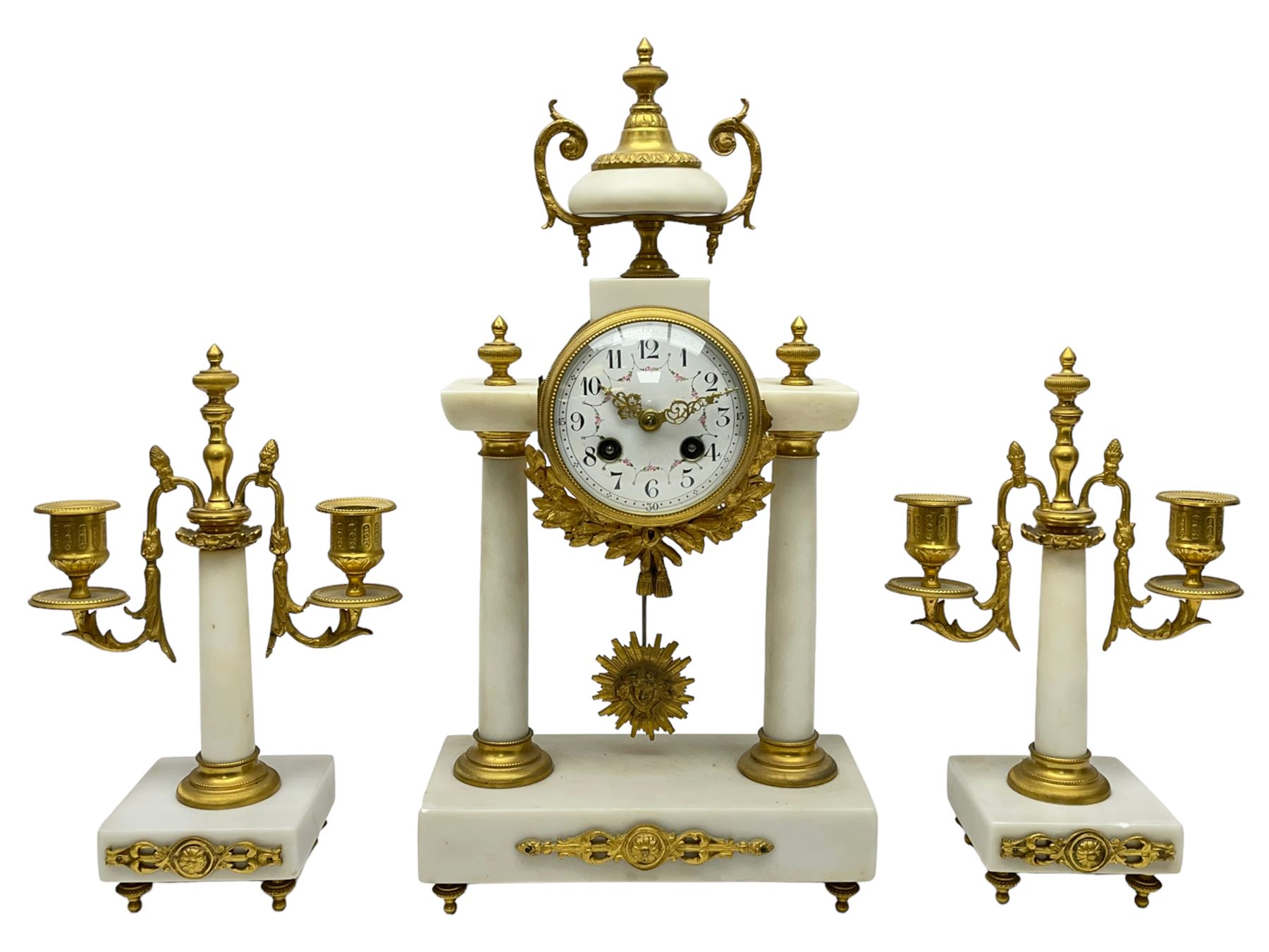 French - Late 19th century 8-day white marble and gilt metal portico clock garniture, the clock surmounted by an urn and raised on a pair of cylindrical pillars above a rectangular plinth base, white enamel dial with Arabic numerals and floral garlands, twin train countwheel striking movement, striking the hours and half hours on a bell, with a sunburst pendulum and gilt Louis XVI hands, garniture with matching twin light candelabra. With Key.   Candelabra H 30cm.