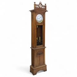 German-Art Deco 8-day longcase clock in an oak case, with a curved top and open fence work pediment, with reeded decoration and a fully glazed case door with a rectangular brass open work panel, on a tall rectangular plinth with a period  carved motif, circular slivered dial with Arabic numerals and spade hands, two train HAC (Hamburg and American Clock Company) weight driven movement, sounding the hours and half-hours on a coiled gong, with weights and pendulum.   