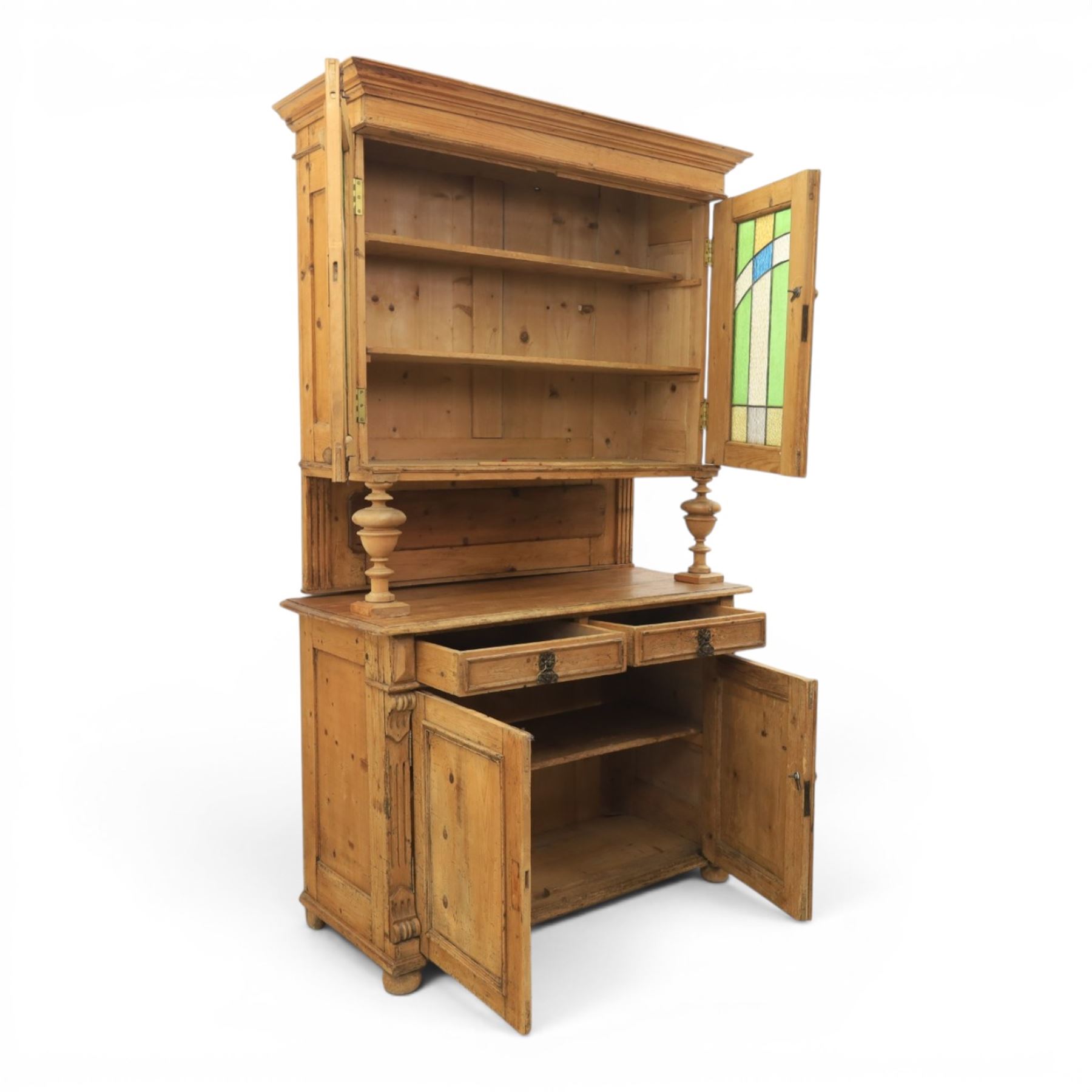 Late 19th century French pine dresser with stained glass upper section, the upper section with projecting cornice with fluted and scrolled details, enclosing a shelved interior, supported on turned front uprights, the lower section with frieze drawers and cupboard doors, raised on bun feet