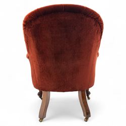 Victorian mahogany framed crimson velvet upholstered tub armchair, with buttoned back and scroll carved arms above a serpentine fronted seat rail, raised upon scroll carved cabriole front legs and plain curved back legs with brass castors 