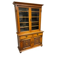 Late 19th century oak bookcase on cupboard, the projecting cornice over two glazed doors and fluted uprights, the cupboard with rectangular moulded top over two drawers and panelled cupboards, the panels carved with scrolling foliage and central cartouche, on turned feet