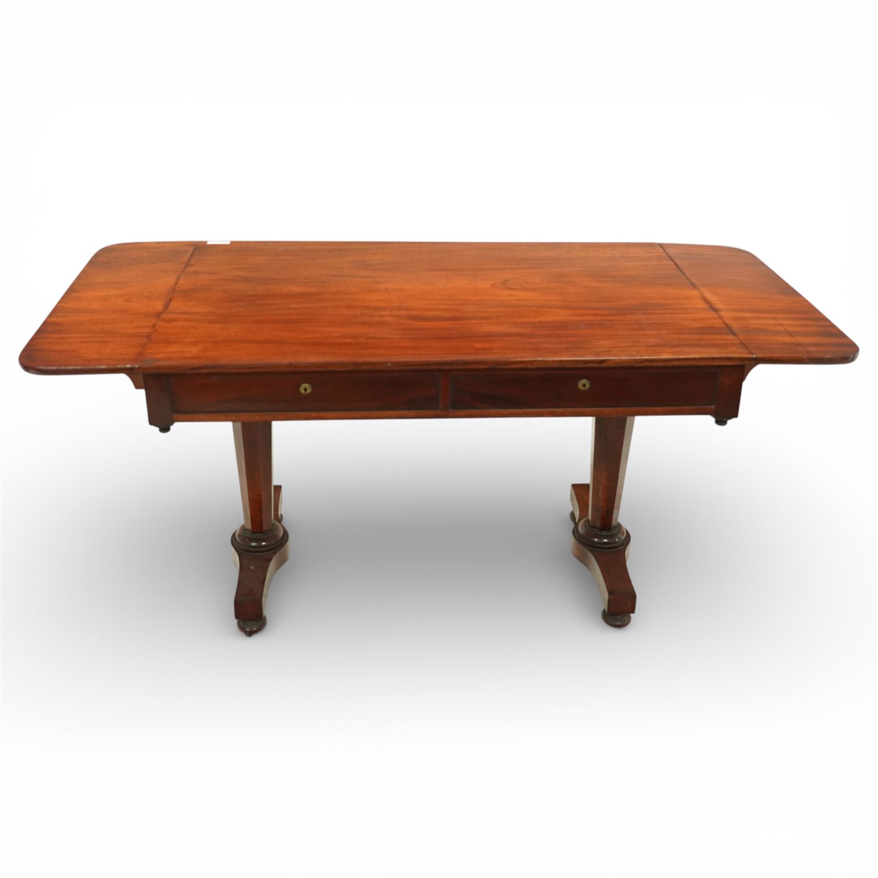 William IV mahogany sofa table, the rectangular top with rounded corners and hinged drop leaves to either end, above a shallow frieze fitted with two drawers opposing conforming dummy drawers, supported on octagonal tapering legs with ring turnings, joined by a shaped stretcher and raised on platform bases with scroll feet