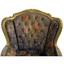 Pair of Louis XVI design gilt framed wingback armchairs, cresting rail carved and moulded with foliate decoration and C-scrolls, upholstered in buttoned floral patterned mauve velvet with loose seat cushion, scallop carved apron over cabriole supports