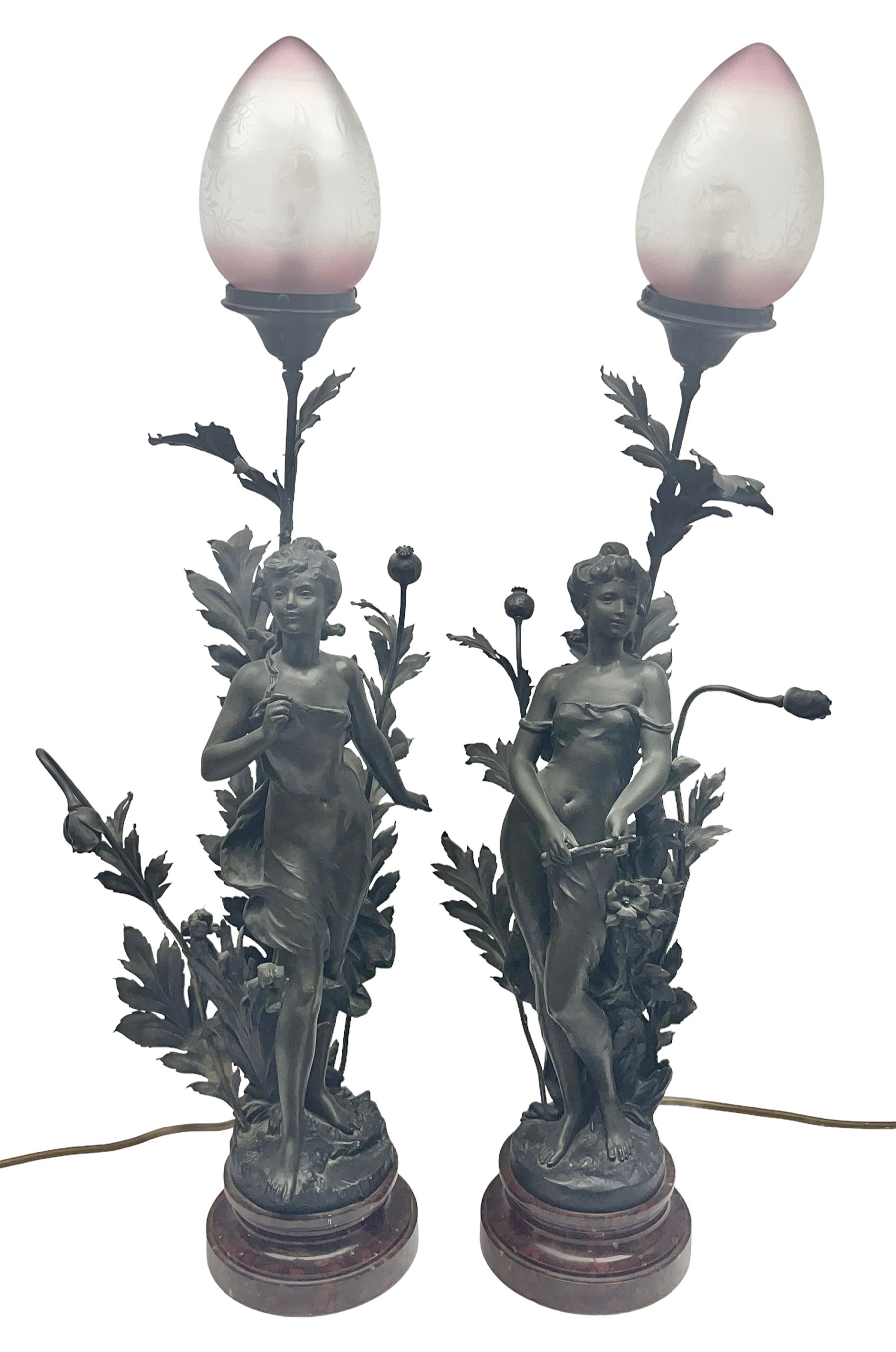 Pair of Art Nouveau style spelter figural table lamps, each mounted on rouge marble effect circular bases, with toleware flower heads and leafy decoration surrounding a female figure, H90cm