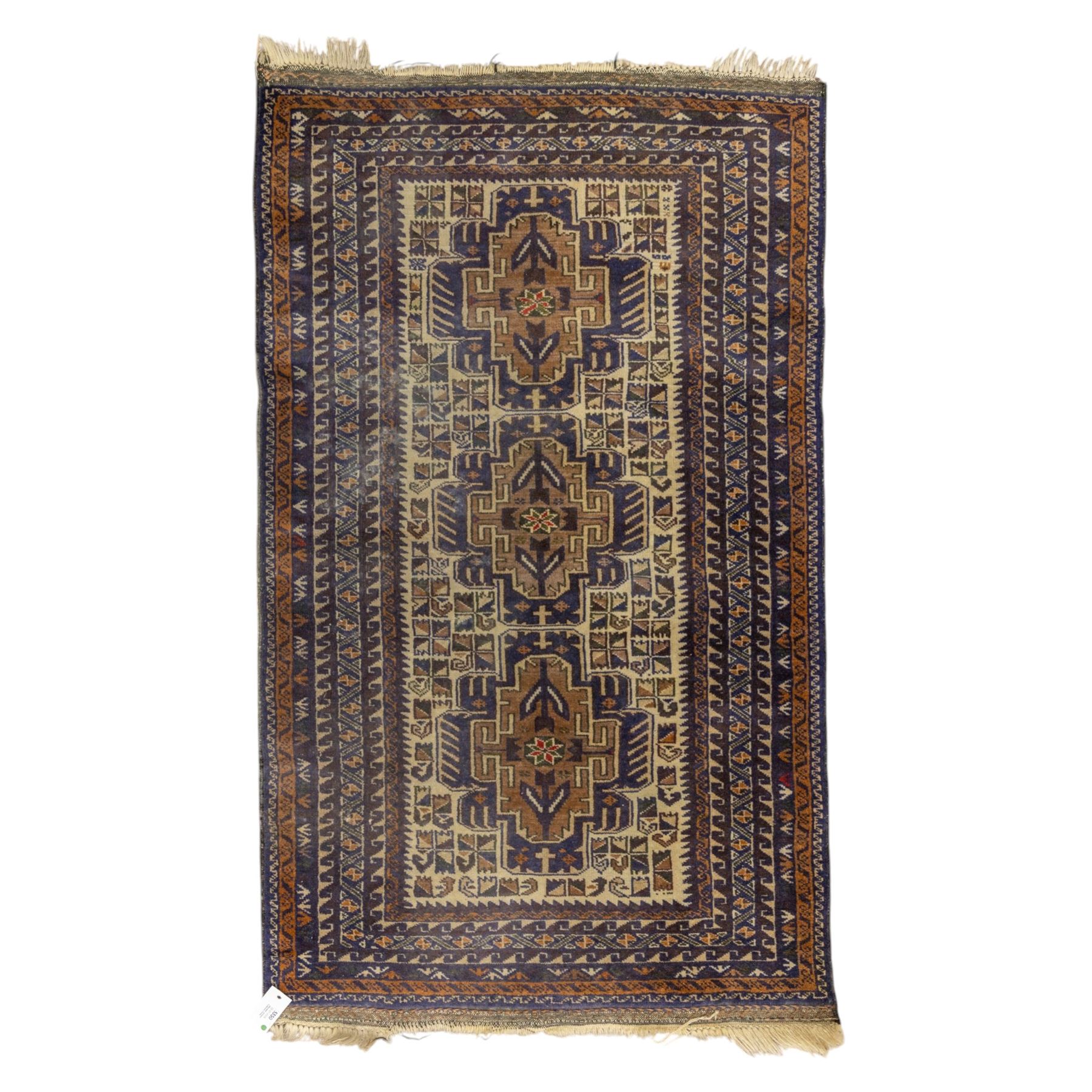Baluchi design wool rug, with three geometric medallions on a cream field, enclosed by multiple dark blue, brown and rust geometric borders with fringed ends