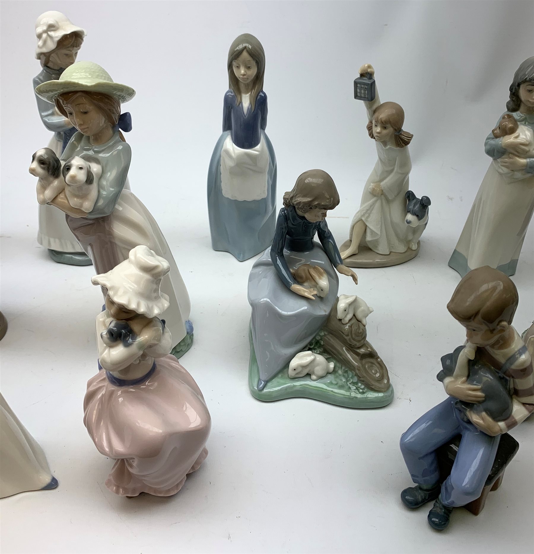 A group of thirteen Nao figurines, together with one Lladro figurine, each with printed mark beneath. 