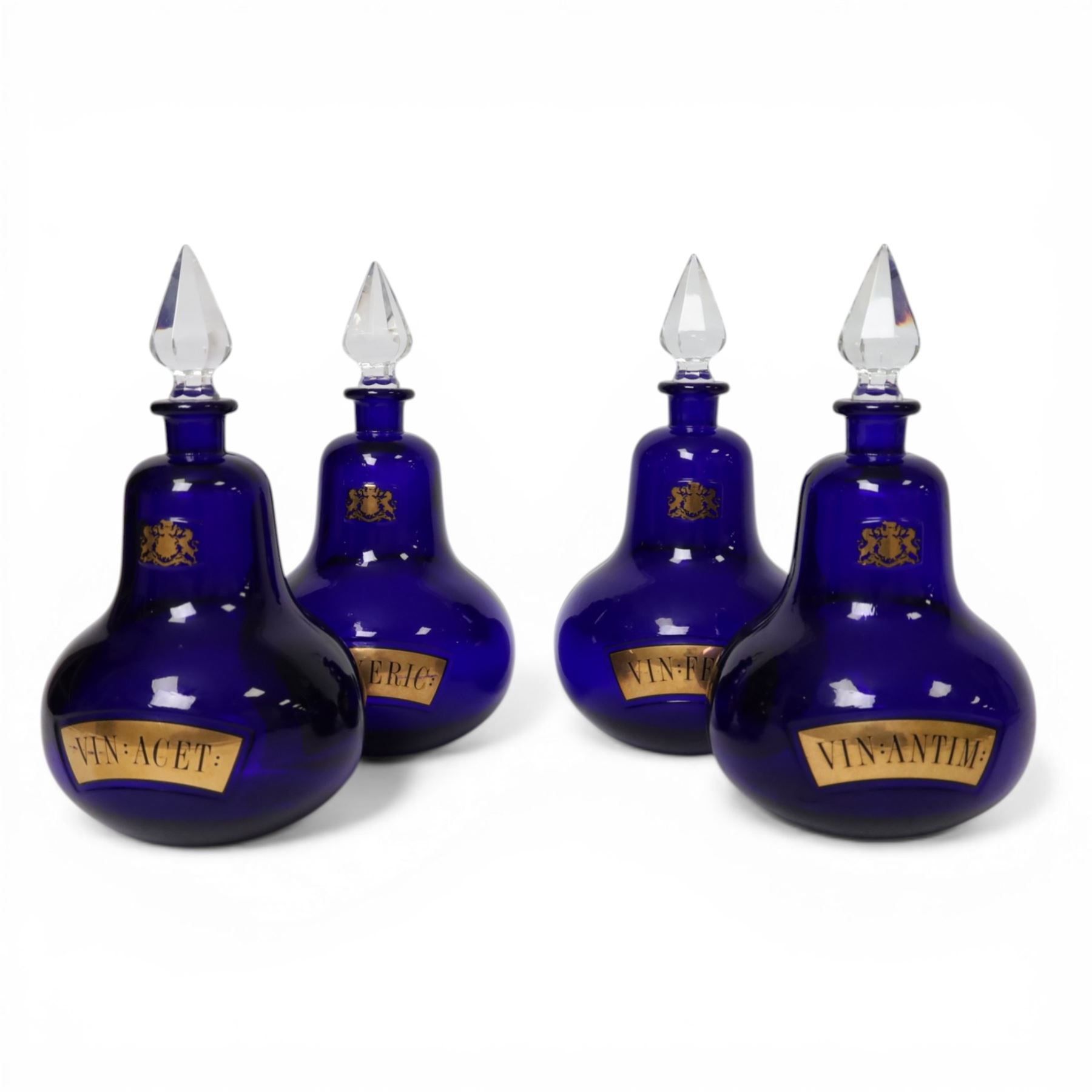 Set of four 20th century Royal Pharmaceutical Society blue glass bottles, of bellied form with clear cut glass spire stopper, each body bearing gilt label in Latin: VIN:ACET:, VIN:ANTIM:, VIN:XERIC:, and VIN:FERR:, and gilt Royal Pharmaceutical Society crest to neck, H25cm

Provenance: From the collection of the family of Peter Green, a practising pharmacist whose career spanned the mid to late 20th century. During his professional life he managed pharmacies in Yeovil, Somerset, and later Selles Chemist in Filey, North Yorkshire, before purchasing and running his own business, Peter Green Pharmacy, located in the Market Place, Malton. The bottles were displayed as part of the traditional shop fittings in both the Filey and Malton pharmacies and were retained as part of his collection.