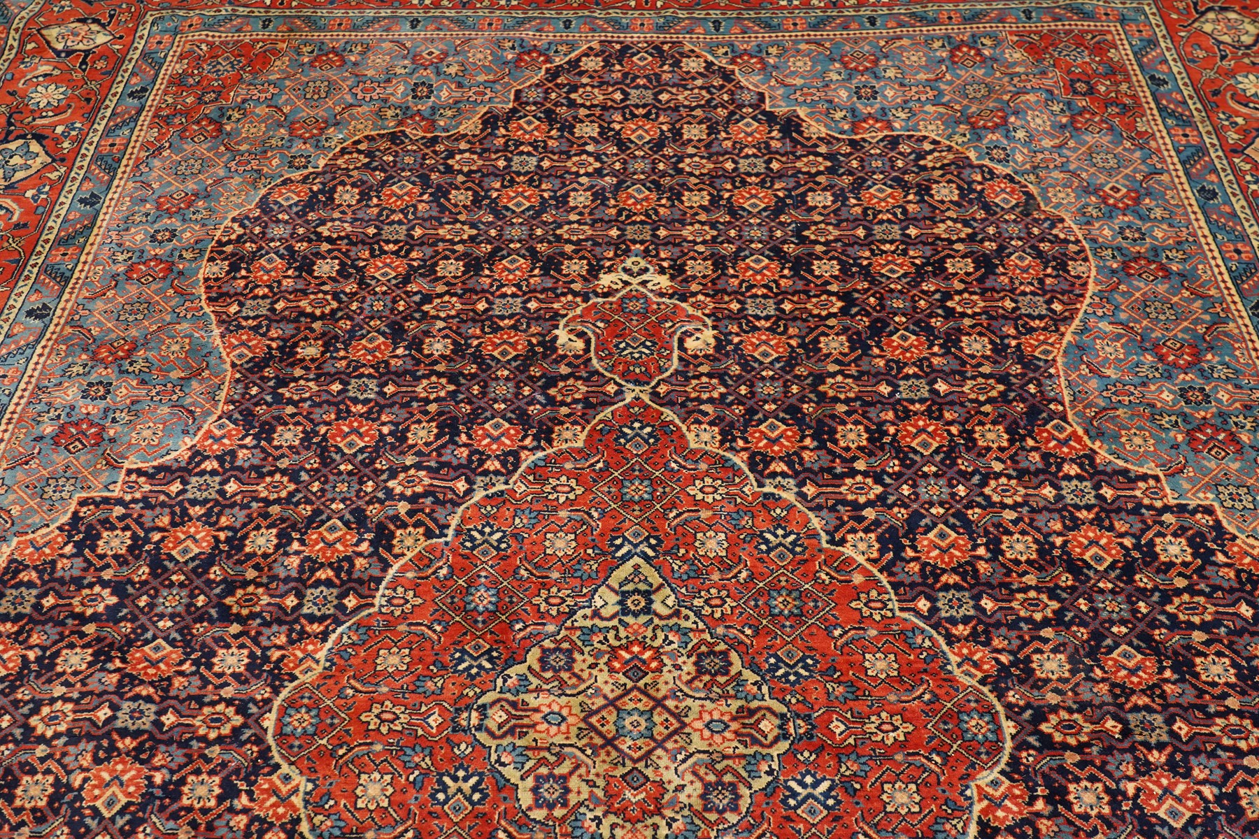 Persian indigo ground Herati rug, the busy field with a central lozenge pole medallion surrounded by repeating Herati motifs, within a shaped spandrel border the crimson guard band decorated with repeating palmette motifs