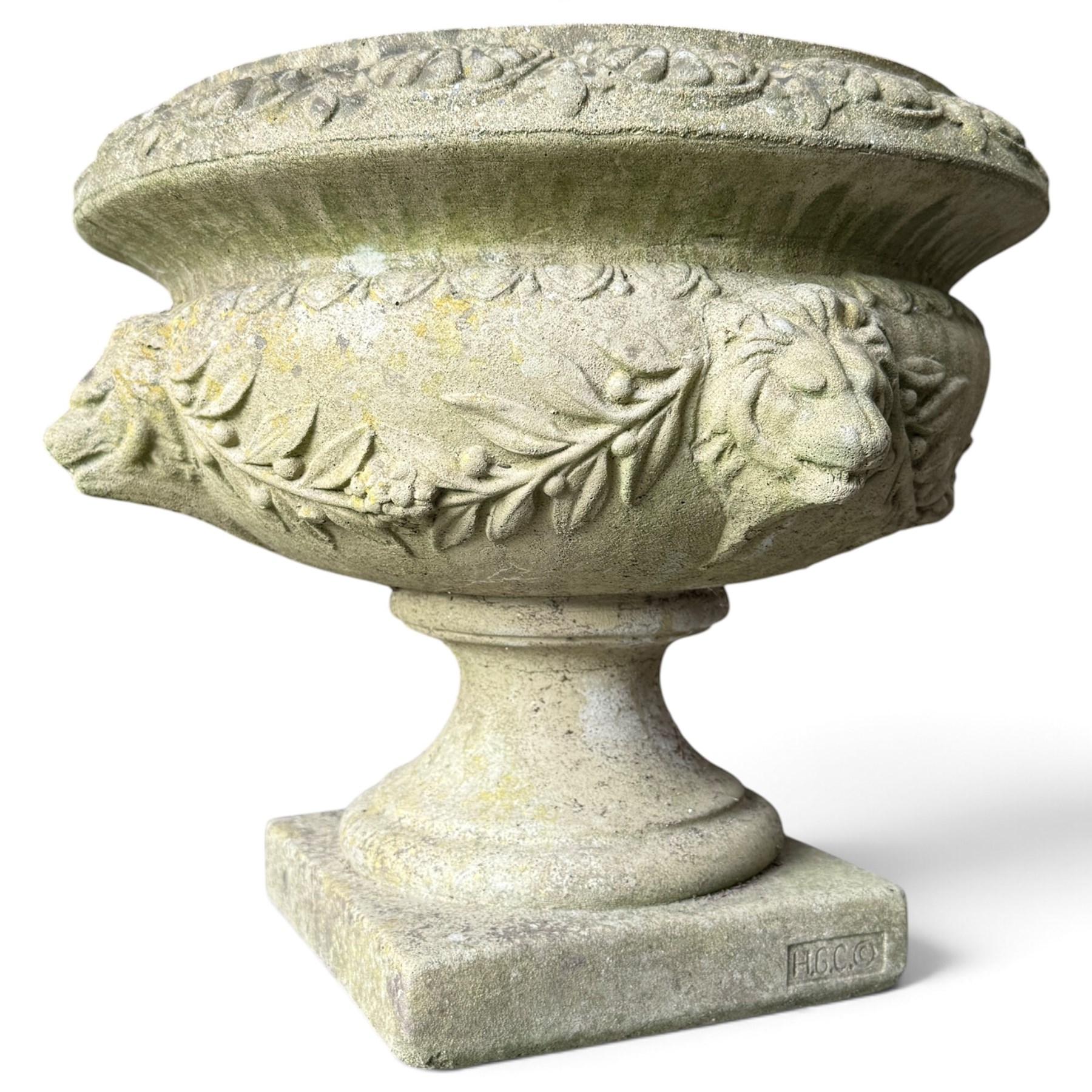 Regency design weathered cast stone garden urn of kylix form, the anthemion and arrowhead moulded everted rim over a fruiting laurel and lion-mask relief decorated body, waisted socle on square base, stamped HGC
