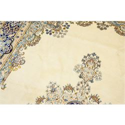 South East Persian Kirman hand-knotted carpet, ivory field with central floral medallion in tones of cobalt and pale blue, issuing scrolling vinery and palmettes, conforming spandrels, main border with scrolling foliage and stylized palmettes, framed by multiple guard borders, with cotton fringe ends 