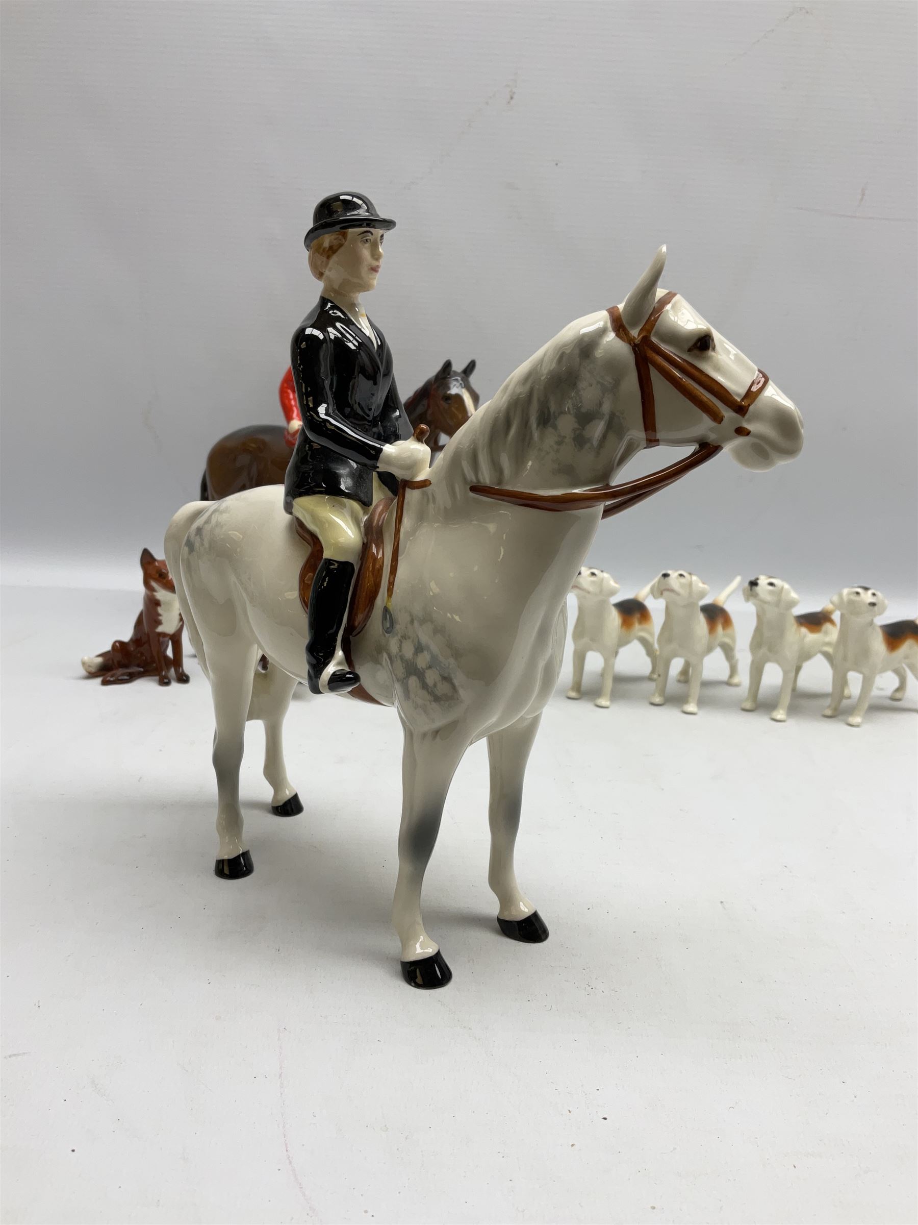 Beswick hunting group, comprising huntswoman on grey horse no 1730, huntsman on brown horse no 1501, two seated fox figures no 1748 and seven fox hounds, all with printed marks beneath (11)