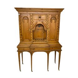 20th century pine architectural collector's cabinet on stand, projecting dentil cornice over various compartments, central recessed arch with turned pillar supports and sloped arch pediment, fitted with four cupboards, false brickwork uprights to front and corners, central hidden drawer revealing cube work surface, lower moulded plinth, the stand with foliate carved mouldings, on six square tapering supports with brass castors