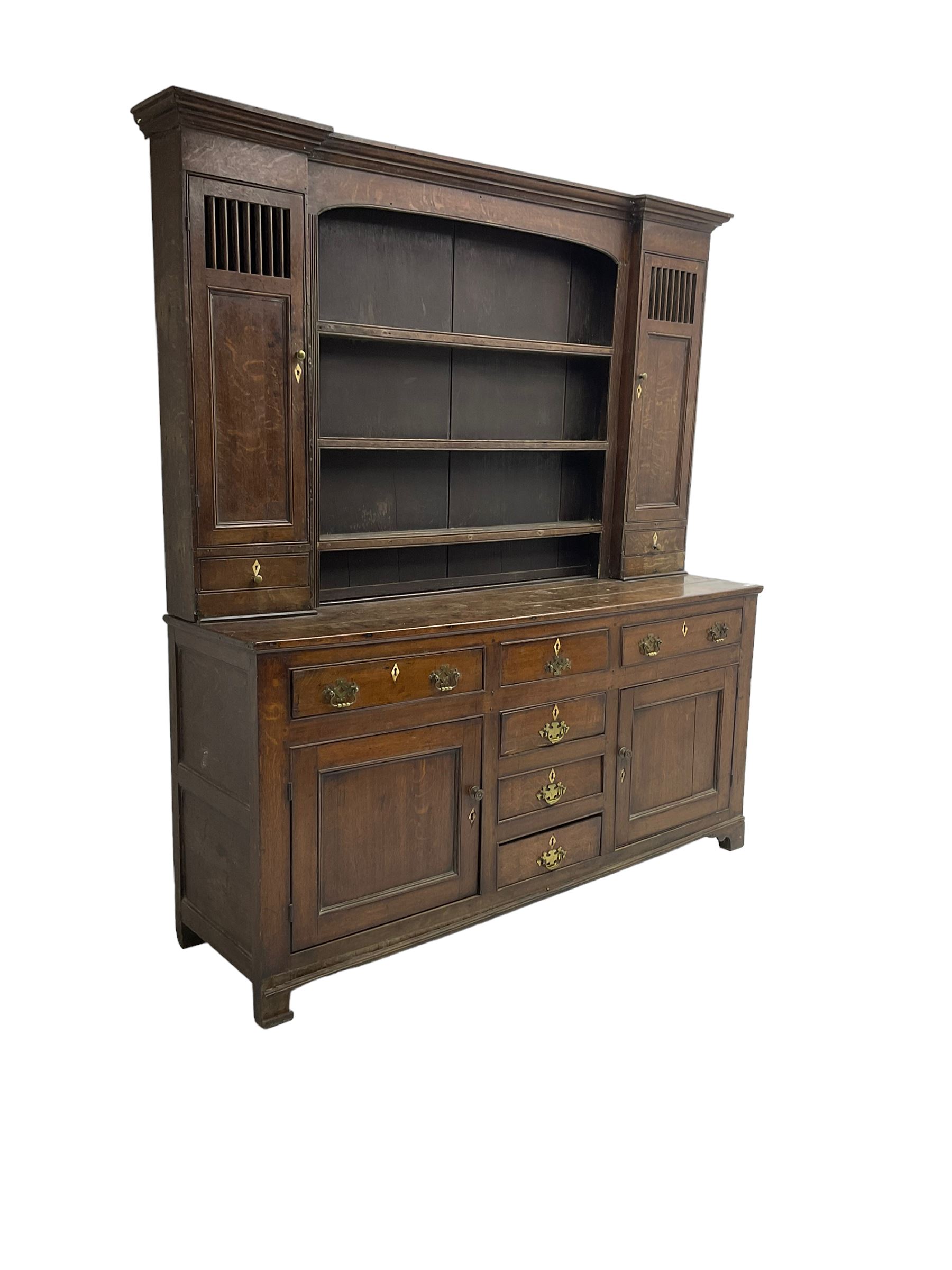 George III oak dresser, projecting cornice over three tier plate rack flanked by reeded uprights and two cupboards, enclosed by slatted and panelled doors above small drawers, the lower section fitted with six drawers and two cupboards, on bracket feet