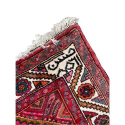 Persian Hamadan red ground rug, decorated with six stepped lozenge medallions, the guarded border with repeating stylised flower head decoration, with inscription to corner