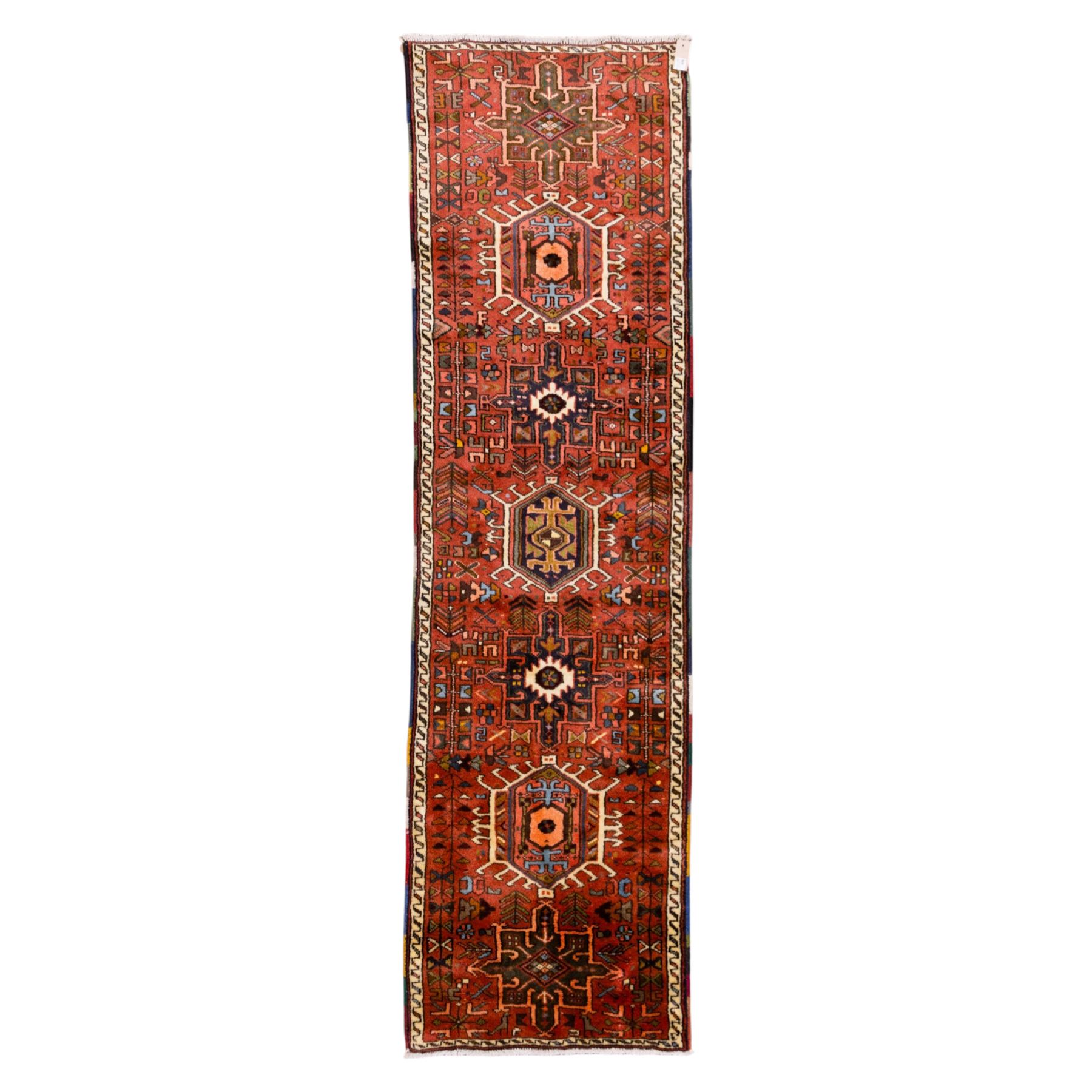 North West Persian Heriz hand-knotted runner, terracotta field decorated with a series of large angular medallions with stylized geometric motifs, surrounded stepped devices, and stylized trees within narrow geometric border, and polychromed edge, cotton fringe ends 