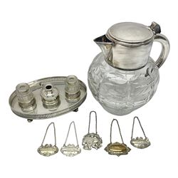 Silver plated lemonade/cocktail jug, the cut glass body with graduating oval decoration and glass ice cube holder to interior, together with a silver plated desk stand, with two faceted glass inkwells and chamberstick and five silver plated decanter labels