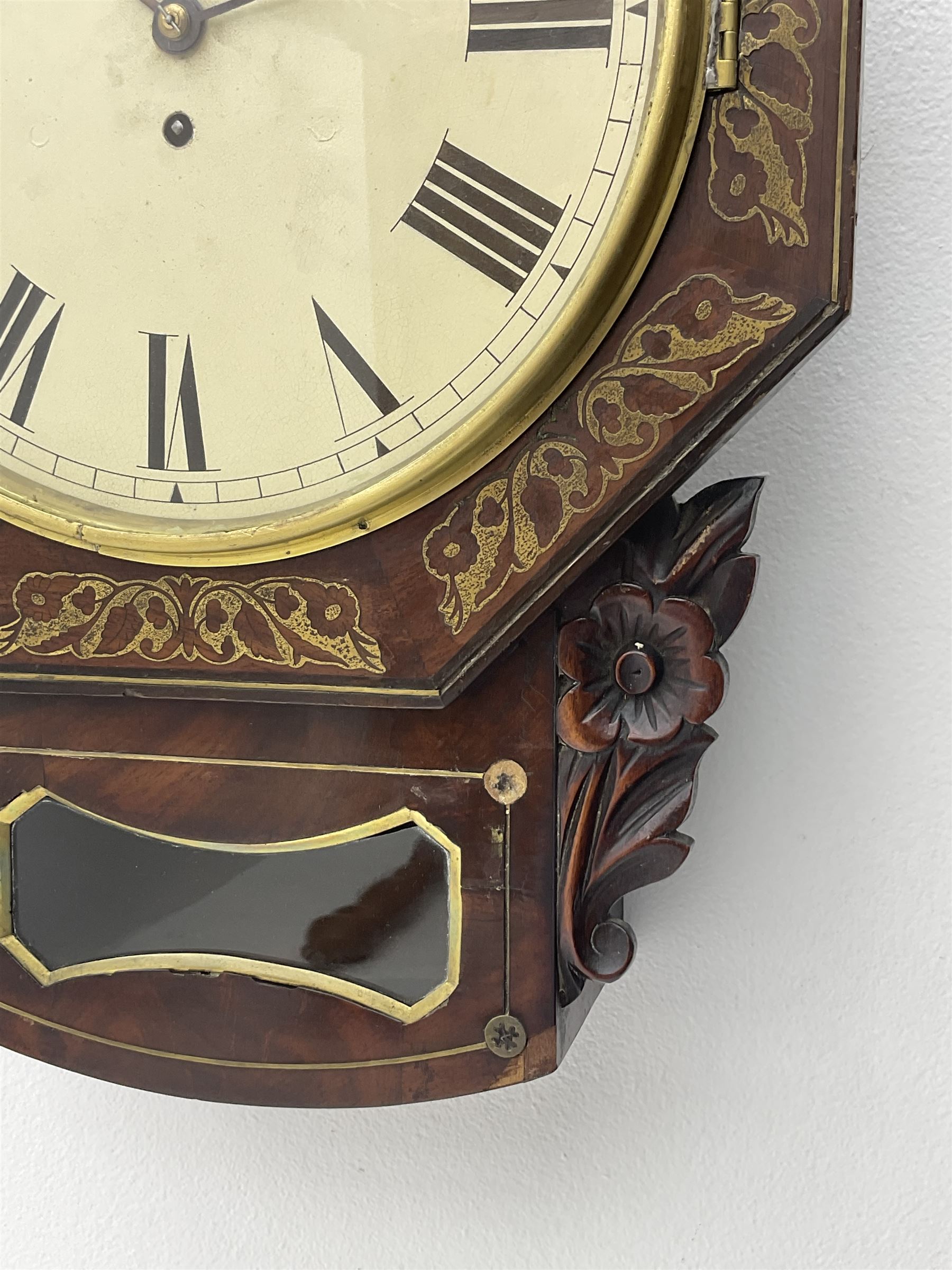 Mid-19th century mahogany veneered eight-day four-pillar single fusee drop dial wall clock with an octagonal dial surround and scroll brass inlay, circular painted steel dial with roman numerals and minute track, matching trefoil steel hands, brass bezel with a flat glass, curved trunk with brass inlaid circles and stringing around the glass pendulum aperture with a brass slip, carved ear pieces in the form of flowers and leaves, with pendulum adjustment door and movement door. With Pendulum & Key