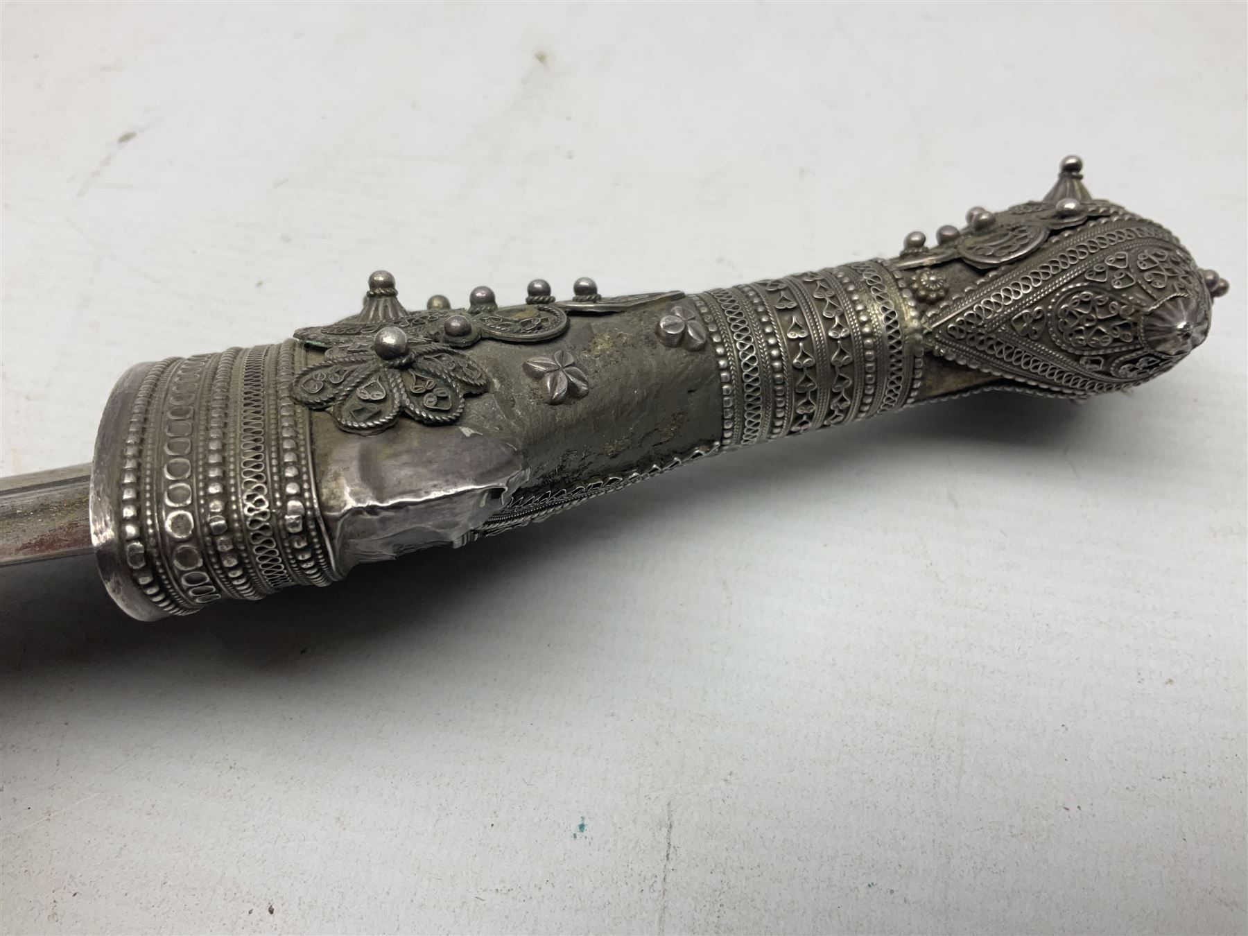 Omani Khanjar dagger, the 19cm curved blade with pronounced medial rib to either side, waisted hilt with dome shaped pommel and silver covered horn grip decorated with filigree bands, floral motifs and beadwork; in an intricately filigree decorated silver and leather scabbard with silver rings woven into the belt mount and fitted with original silver thread-work belt L34cm overall belt length 94cm