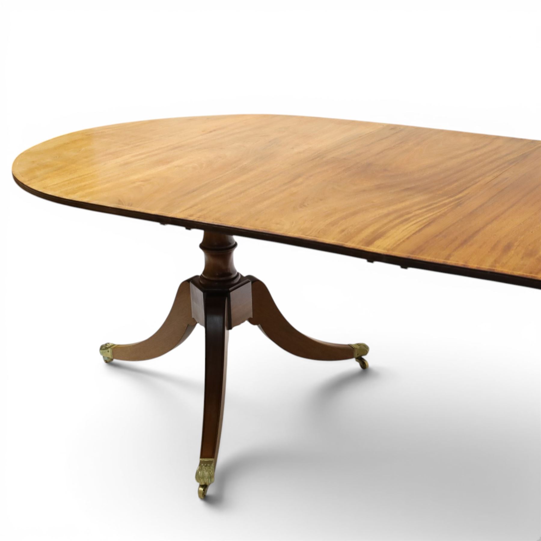 Acornman - mahogany twin pillar extending dining table, strongly grained top with inlaid edge, raised on a ring turned baluster column, above three swept supports terminating in brass paw feet above castors, two additional leaves extending the table to 242cm, with signature carved acorn, by the workshop of Alan Grainger of Brandsby