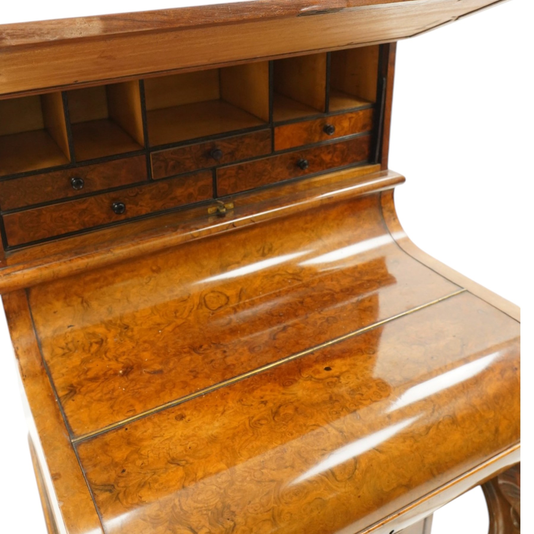 Victorian burr walnut piano-top Davenport, the raised rectangular superstructure with moulded cornice above a panelled fall-front enclosing drawers, the curved hinged writing slope opening to reveal a fitted interior above a sliding tooled leather writing surface, flanked by carved foliate scroll supports, the right side fitted with four drawers behind an arched panelled cupboard door with brass inset campaign-style handles, on a shaped plinth base and bun feet