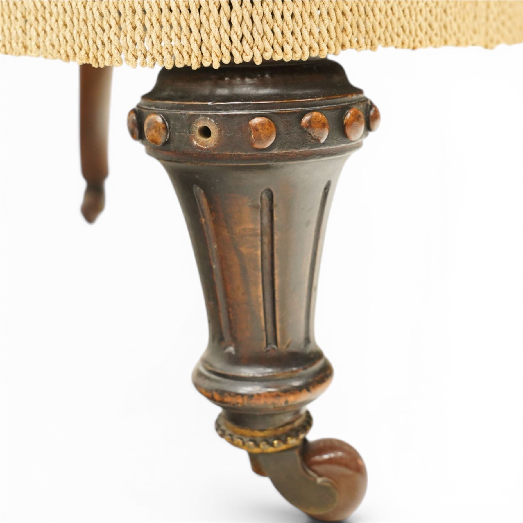 Victorian Aesthetic Movement walnut framed nursing chair, the fan back and sprung seat upholstered in buttoned foliate patterned gold damask fabric with fringing, raised on beaded tapering fluted supports with ceramic castors