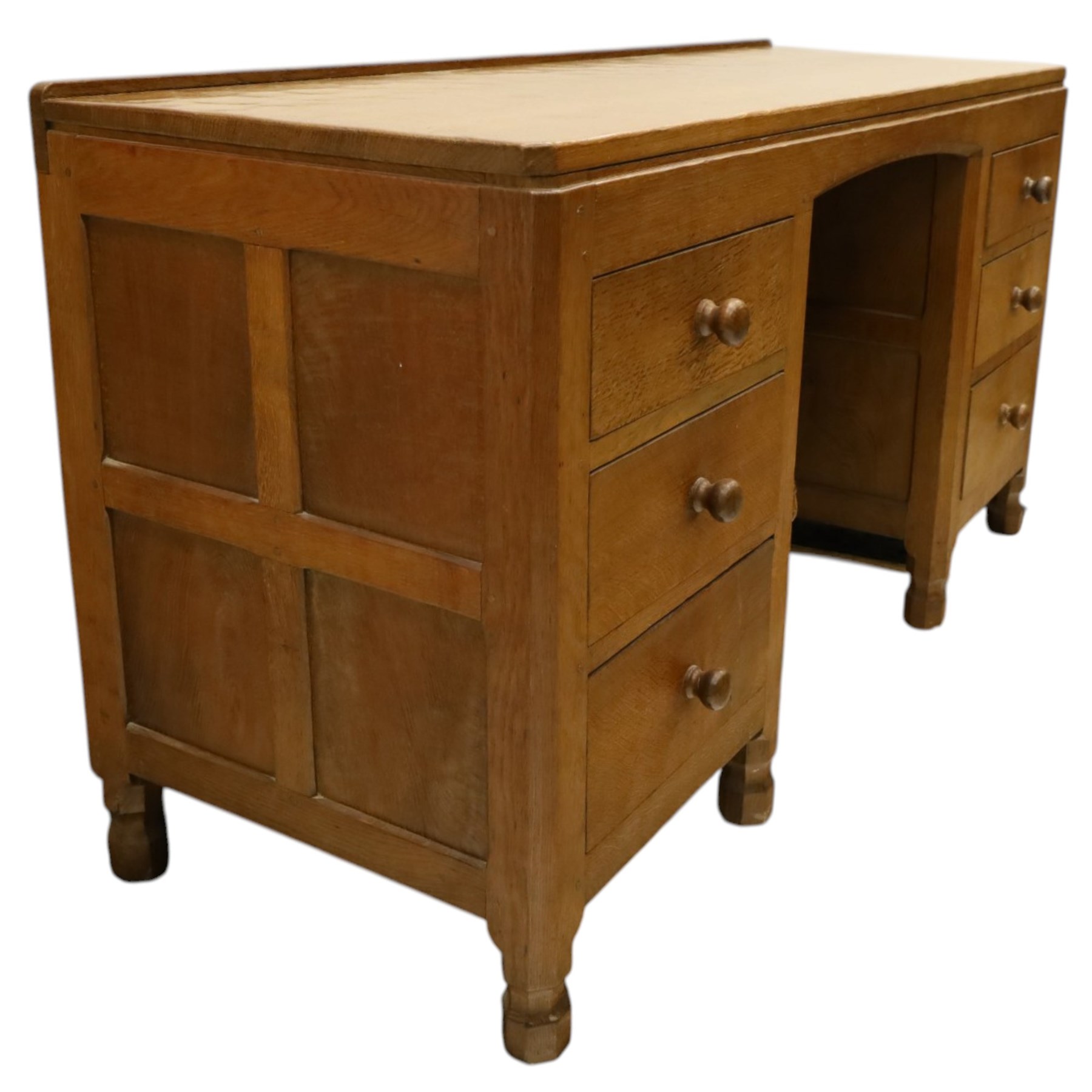 Mouseman - adzed oak kneehole dressing table or desk, the rectangular adzed top with raised back and canted corners, over an arched recessed kneehole flanked by three graduating drawers to each side with turned knob handles, raised on octagonal feet, with carved mouse signature, by the workshop of Robert Thompson of Kilburn