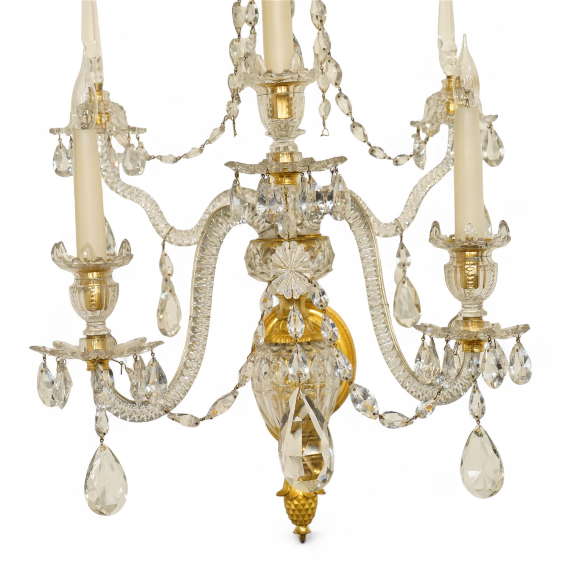 Pair of George III ormolu and cut-glass wall-lights, each with a tall central urn-shaped finial above a series of faceted glass spires and scrolled branches, the ormolu-mounted nozzles and drip pans hung with festoons of cut-glass drops and pear-shaped pendants, the lower section centred by a pineapple finial, wired for electricity