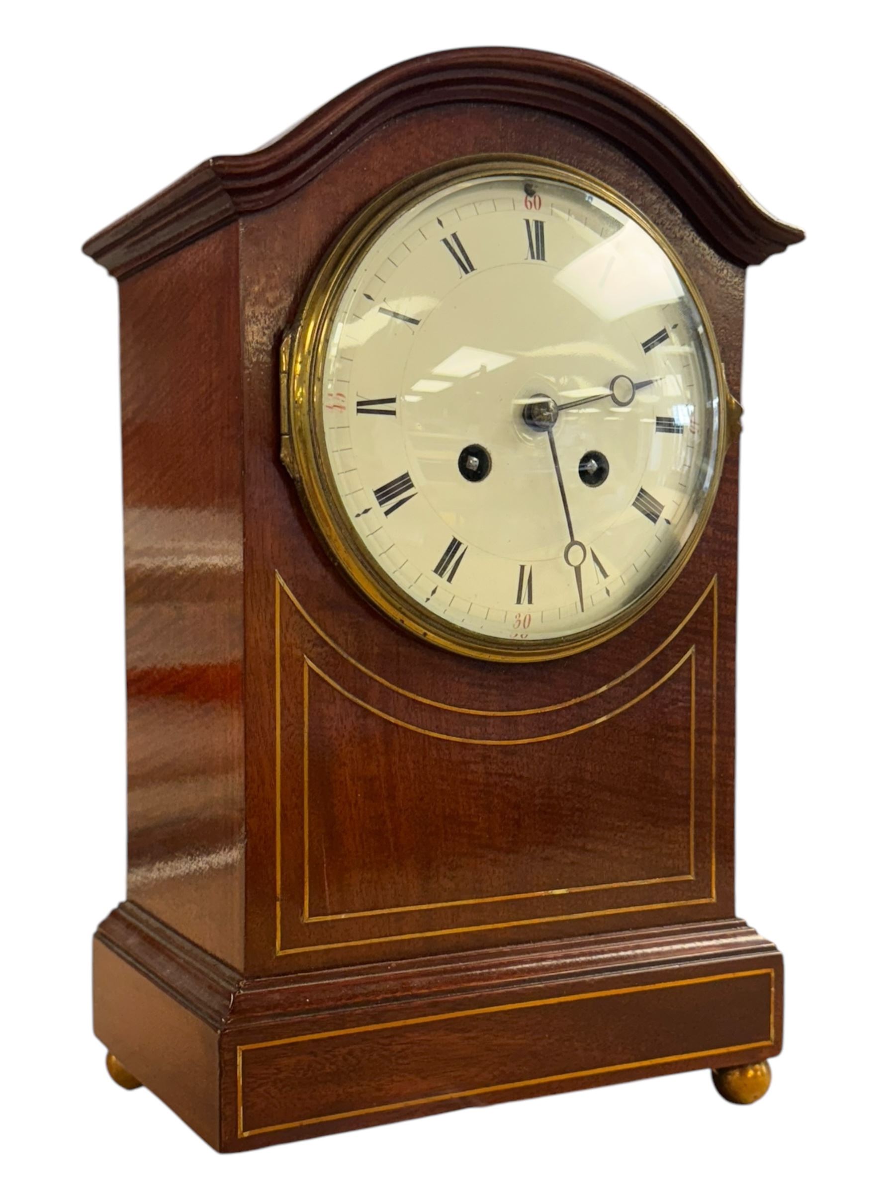 Edwardian-French 8-day mantle clock in a mahogany case with satinwood inlay, on a narrow plinth raised on ball feet, enamel dial with Roman numerals and steel moon hands, rack striking movement, sounding the hours and half hours on a gong. With pendulum and key.