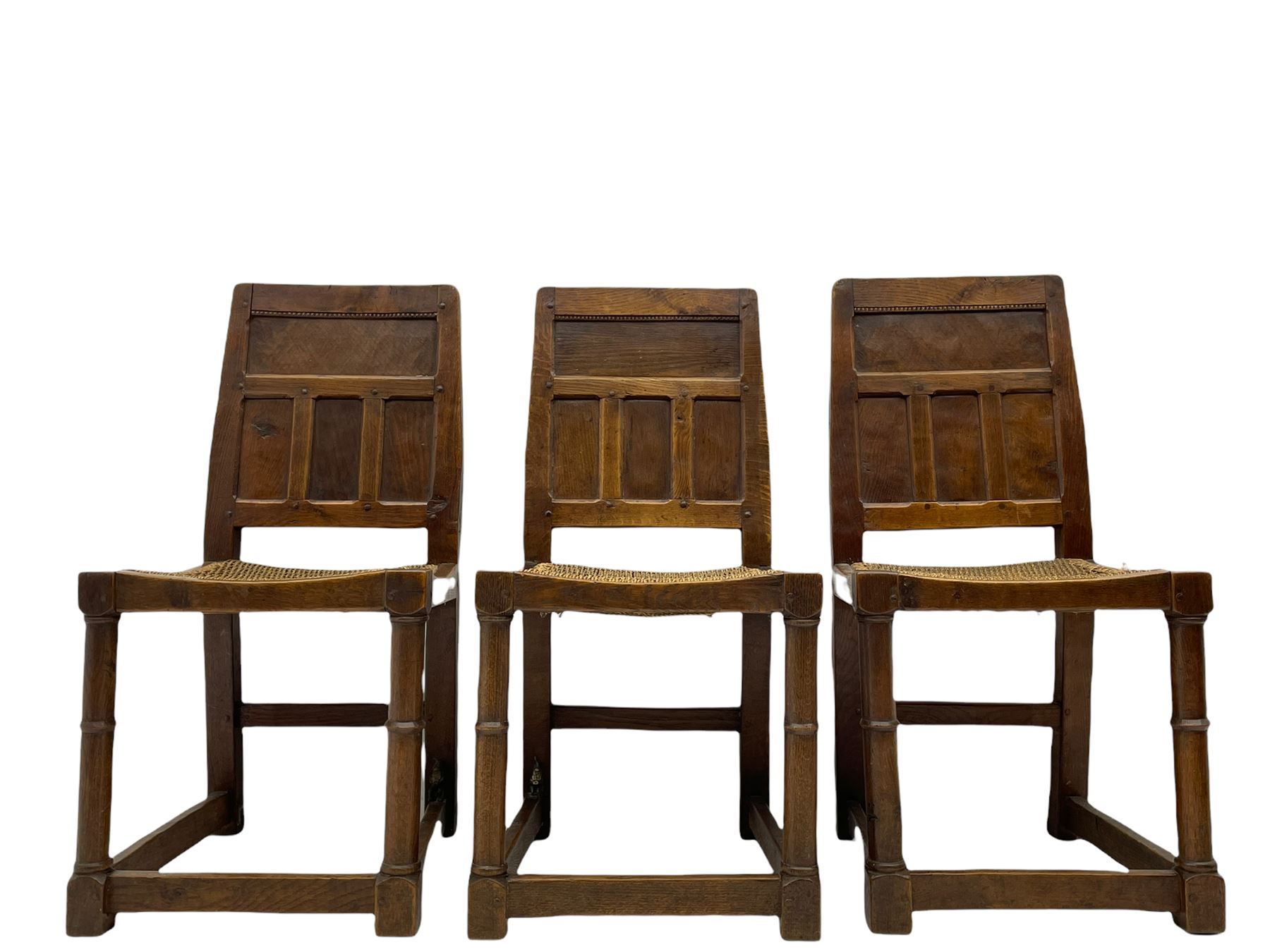 'Gnomeman' set of three oak dining chairs, panelled backs over curved seat rails with drop in rope rush seats, turned front supports with collar joined by plain stretchers, two with carved seated gnome figures, painted

Provenance - This collection of early 'Gnomeman' furniture comes to us directly from the Whittaker family. The pieces were made by the vendor's father Thomas Whittaker in the 1930/40s for his own use. During this time, he lived in York and made items for himself and friends. Whittaker adopted the gnome as a signature and trademark after his move to Littlebeck, Whitby.