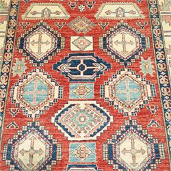 Caucasian Kazak hand-knotted rug, madder red field with bold geometric medallions and angular tribal motifs, within multiple patterned borders in a palette of indigo, red, ivory and green 