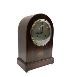 Edwardian - German 8-day mahogany mantle clock with a round top and satinwood inlay to the front, on a shallow base raised on button feet, silvered dial with arabic numerals and spade hands, cast brass bezel with a convex glass, rack striking twin train movement, sounding the hours and half hours on a coiled gong. With pendulum. 