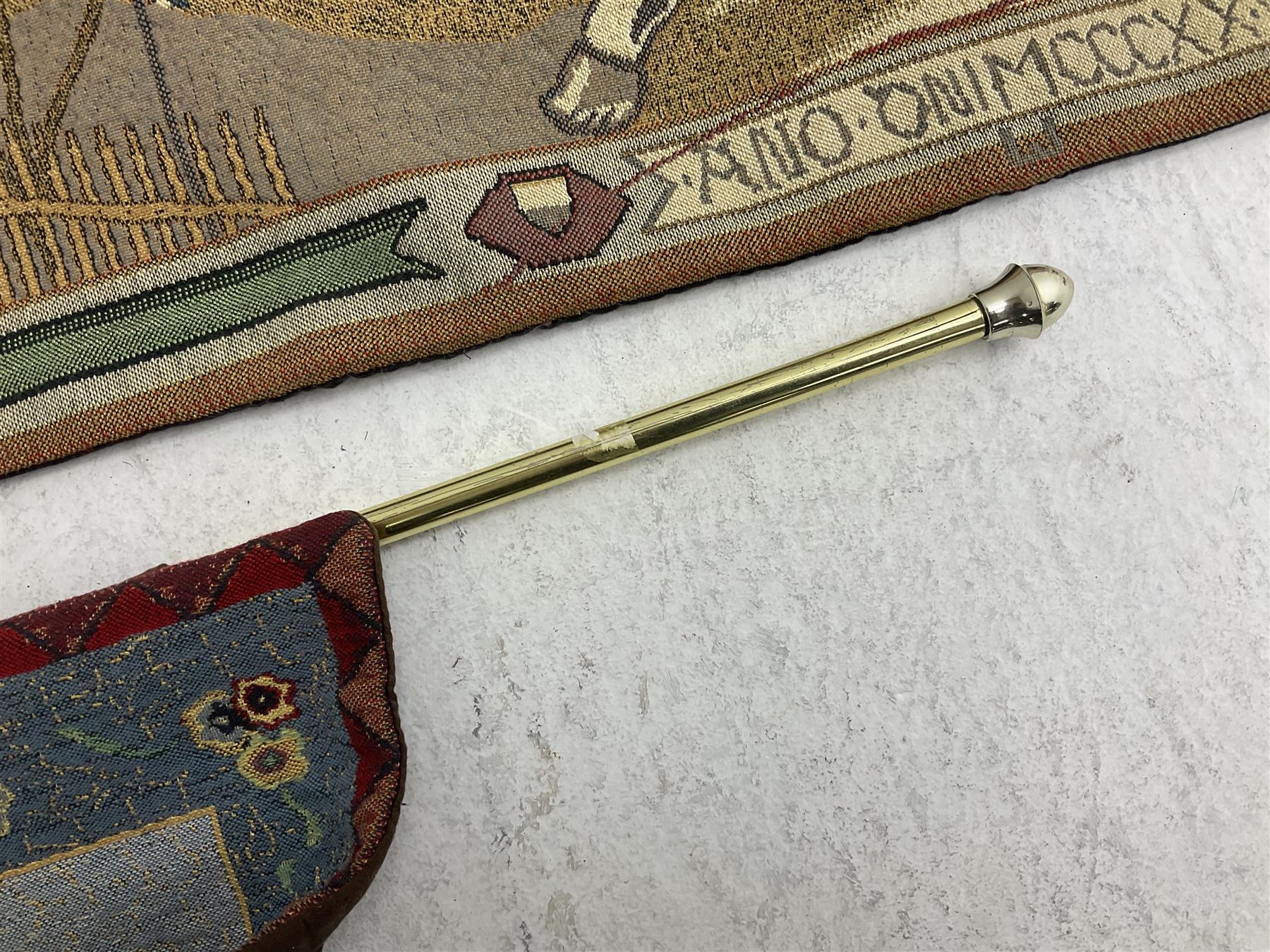 Three tapestries comprising 20th century wool tapestry panel of a medieval nobleman upon a horse with a castle in the distance, together with a smaller tapestry depicting The English Coat of Arms, both hung on rails, and further depicting village scene, largest approx 132cm x 95cm