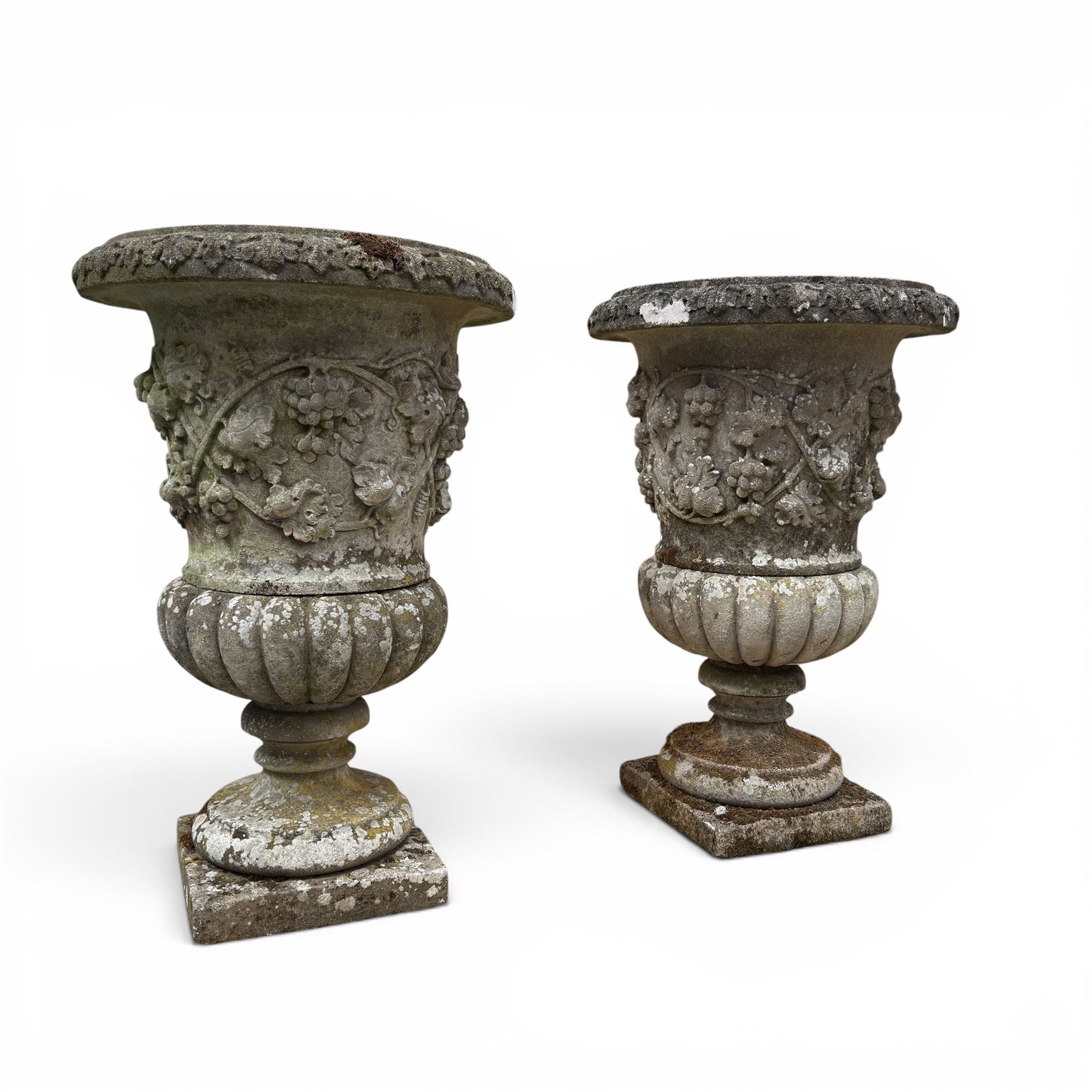 Pair of quality antique weathered three-piece composite stone garden urns, the flared rim moulded with repeating acanthus leaves, over a deep-relief campana body decorated with fruiting grapevines and ivy leaves, the gadrooned underbelly over a turned socle and square base