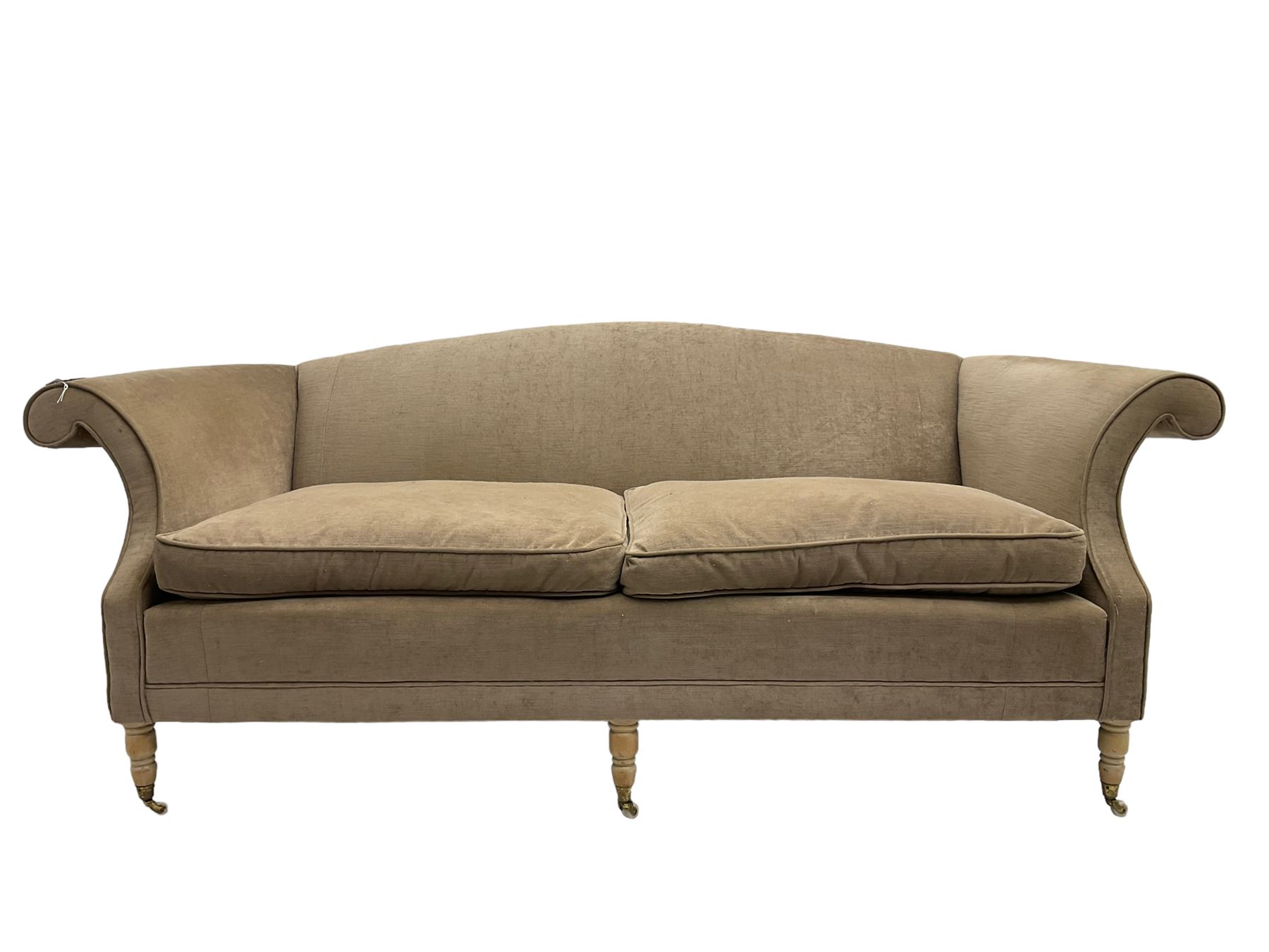 Traditional three seat sofa, curved back over scrolled arms, upholstered in crushed beige fabric with matching loose cushions, on turned front supports with brass and ceramic castors, together with matching footstool