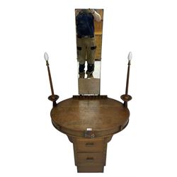 Art deco oak dressing table, raised back with rectangular swing mirror, oval top with flanking electric candlesticks, the frieze with central floral panel and two drawers, over two central drawers