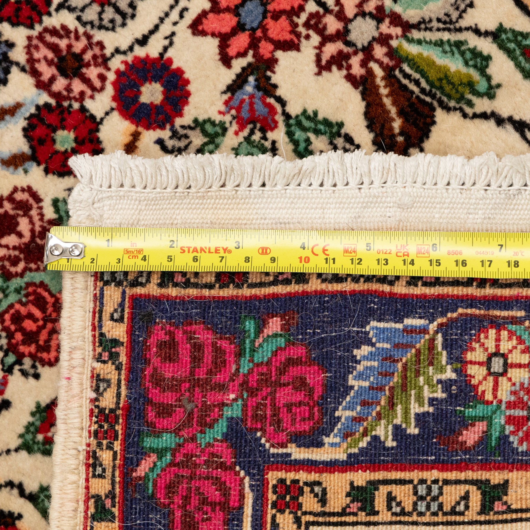 Two small rugs, an ivory ground example decorated with a central floral medallion and scattered rose sprays, enclosed by a navy foliate border (62cm x 101cm), and a crimson pictorial mat worked with seated figures, an animal and birds amongst flowering plants (45cm x 79cm) (2)