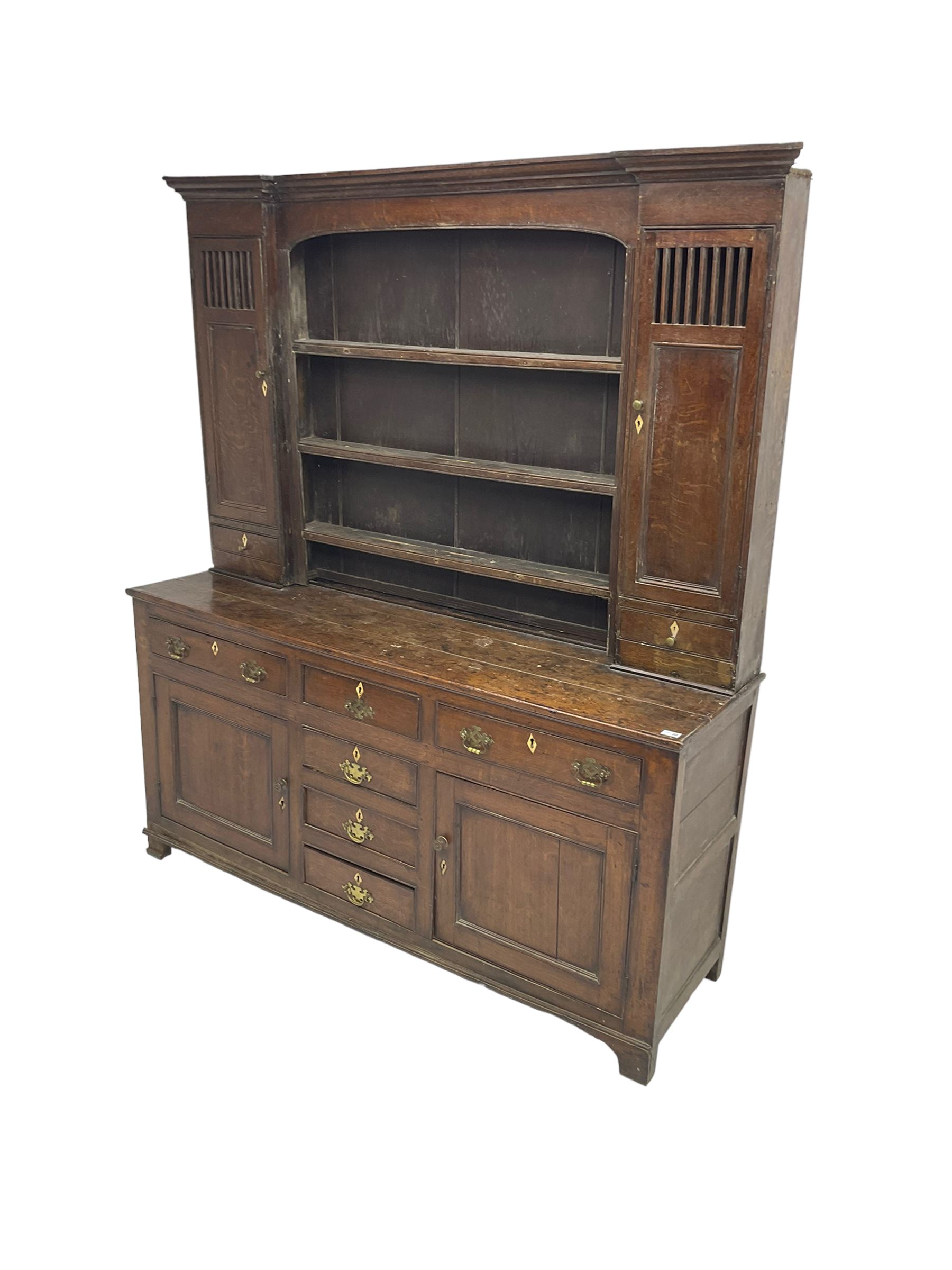 George III oak dresser, projecting cornice over three tier plate rack flanked by reeded uprights and two cupboards, enclosed by slatted and panelled doors above small drawers, the lower section fitted with six drawers and two cupboards, on bracket feet