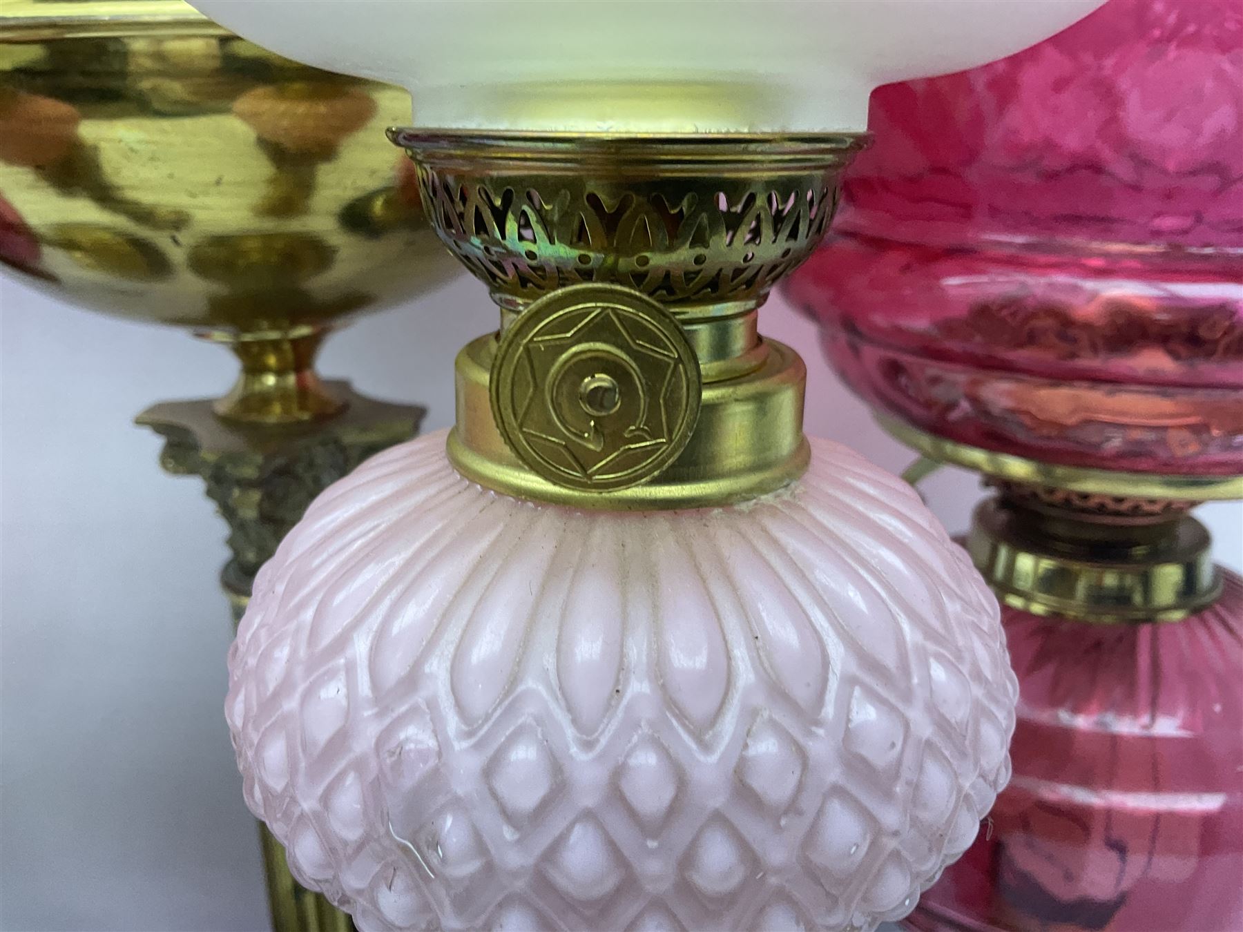 Victorian cast brass oil lamp, with fluted pink glass shade, together with two smaller brass oil lamps with pink shades and reservoirs and a pair of oil lamps, the bases modelled as putti, with pink glass reservoir  and frosted shades, tallest H70cm