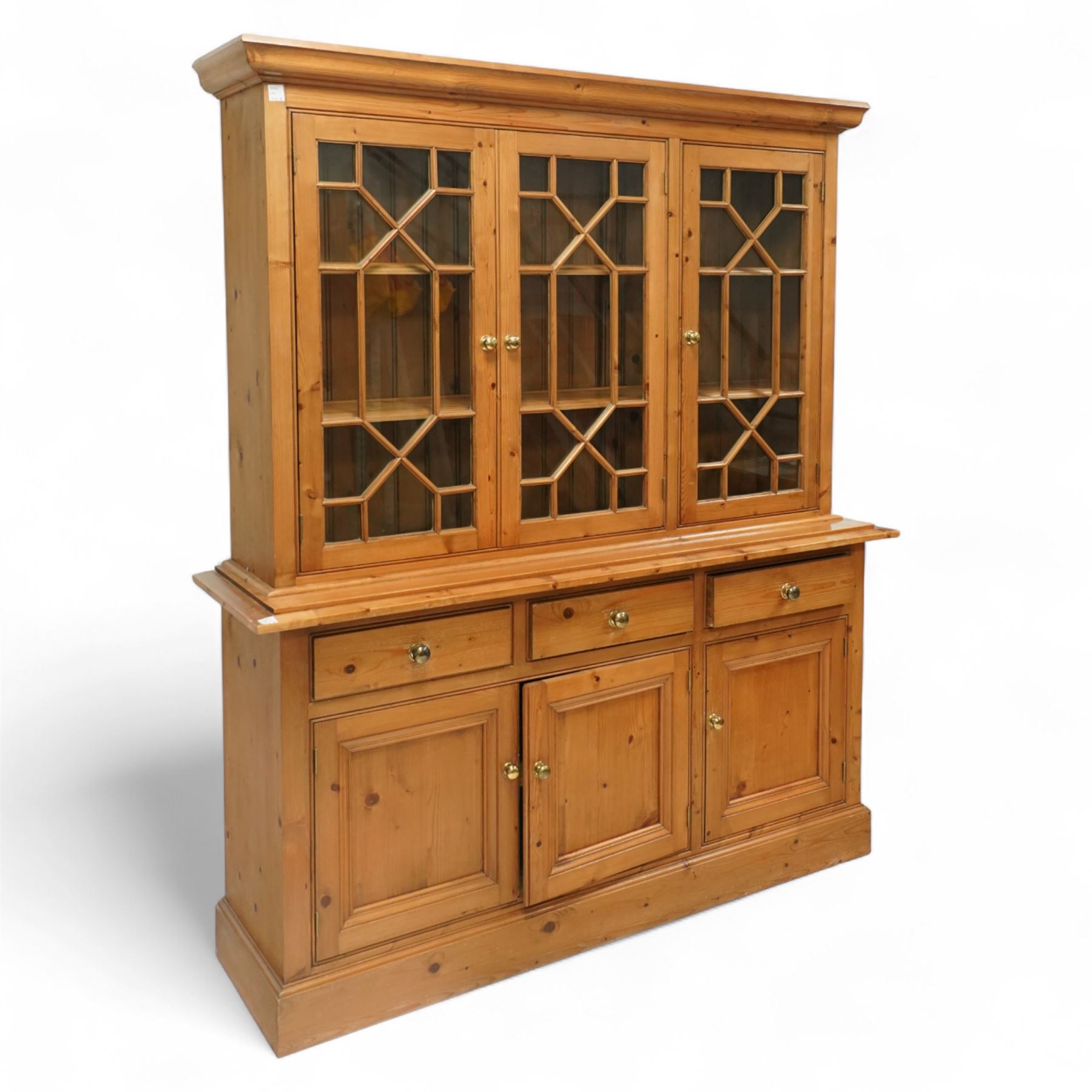 Mid 20th century pine glazed dresser on cupboard base, upper section of rectangular form with three astragal glazed hinged doors enclosing two adjustable wooden shelves and projecting frieze over three short drawers and three hinged panelled cupboard doors with brass handles, the front and sides, raised on a plinth base 