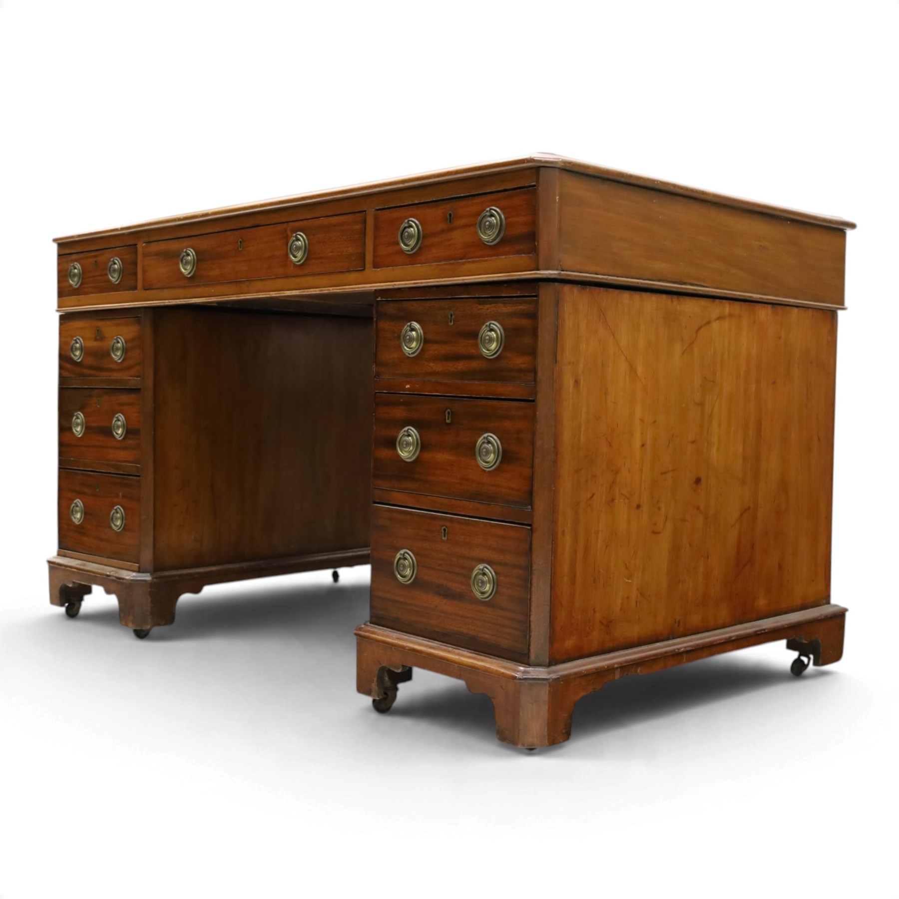Late Victorian mahogany desk with red leather top, rectangular top with inset toold red leather writing surface, central long frieze drawer flanked by two short drawers, above pedestal with three graduating drawers with ring pull handles, on moulded plinth bases raised on castors