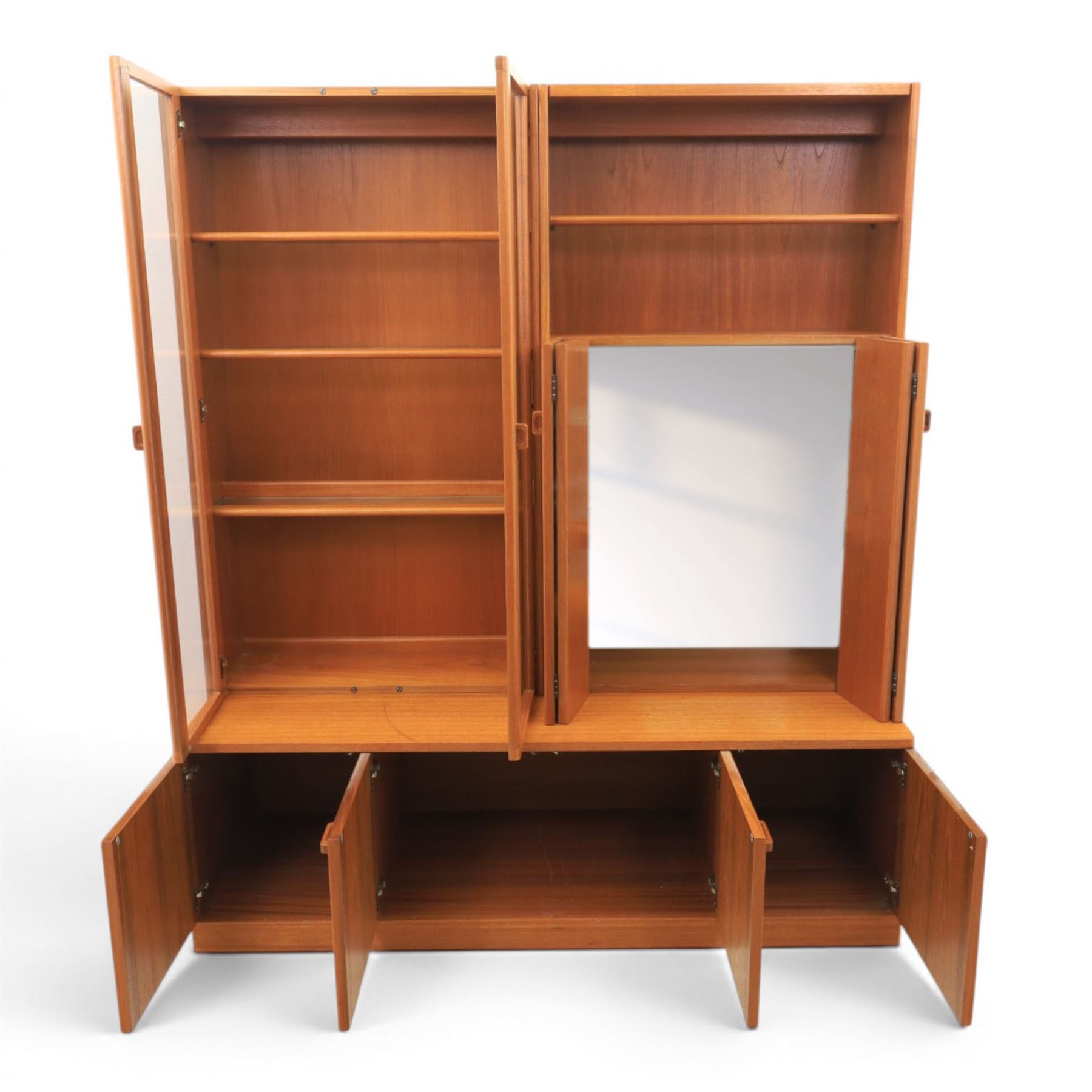 G-Plan - Mid 20th century teak modular wall unit, the upper section fitted with twin glazed doors enclosing shelves, adjoining concertina doors with mirrored and shelved interior, the base with four cupboard doors with recessed rectangular handles, raised on a plinth base