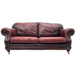 Thomas Lloyd - three-piece lounge suite, comprising of traditional shape two seat sofa (W190cm H80cm) and a pair of wingback armchairs (W100cm H91cm), each with rolled arms over turned supports with brass castors, upholstered in oxblood red leather