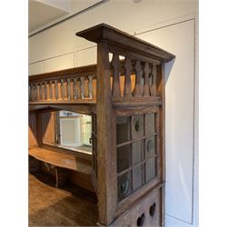 Shapland and Petter - Arts & Crafts period oak dresser, raised gallery top with spade balustrade, central bevelled mirror flanked by two cabinet, astragal glazed doors with yellow tinted glass and bullseye panes, the sides with pierced heart shaped decoration, fitted with two drawers and two double cupboards, enclosed by linenfold panelled doors,  copper work strap hinges and fixtures, on shaped spade feet, the locks stamped 'S&P'